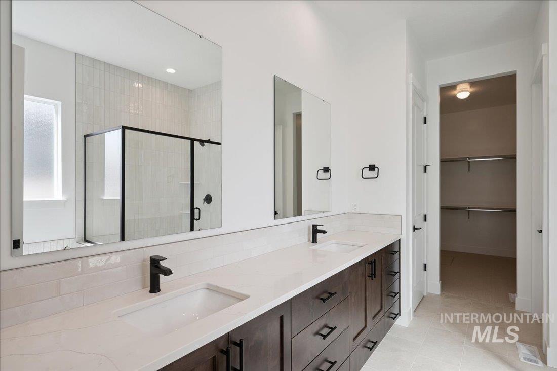 Bathroom featuring a stall shower, double vanity, a walk in closet, and light tile patterned floors