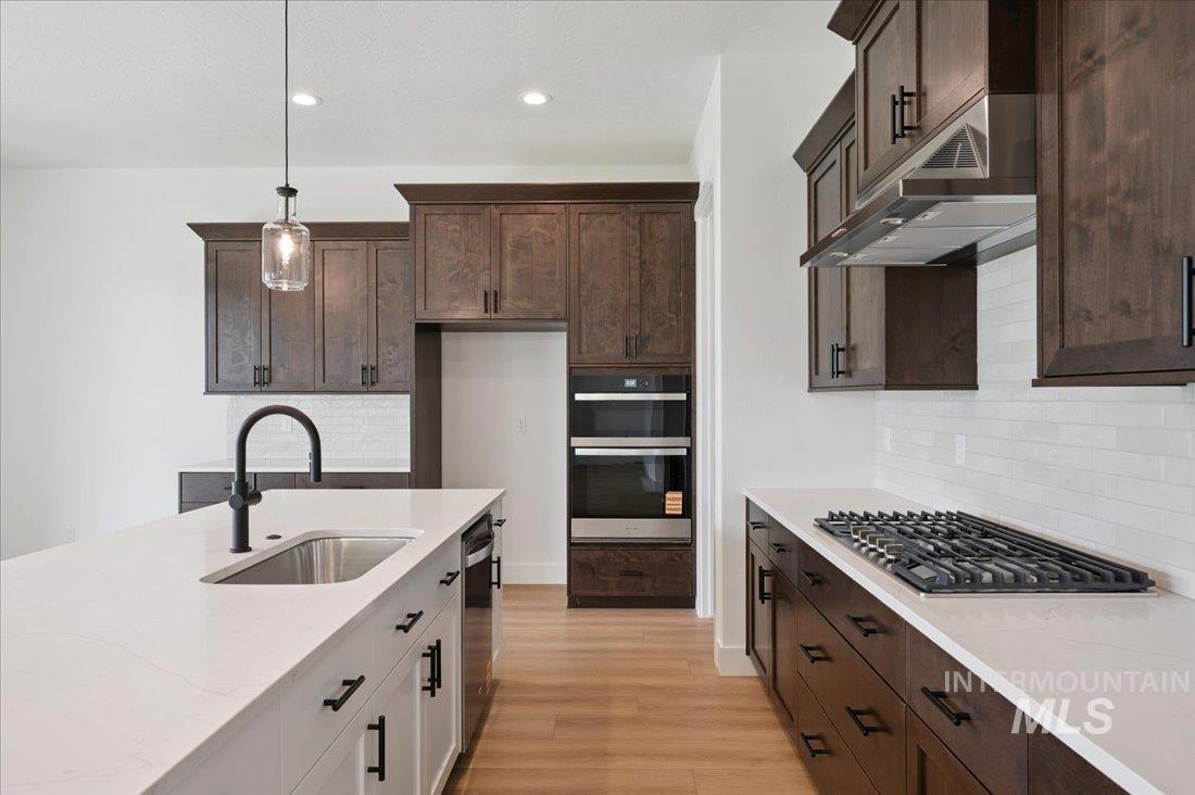 Kitchen featuring light stone countertops, decorative light fixtures, tasteful backsplash, dark brown cabinets, and recessed lighting