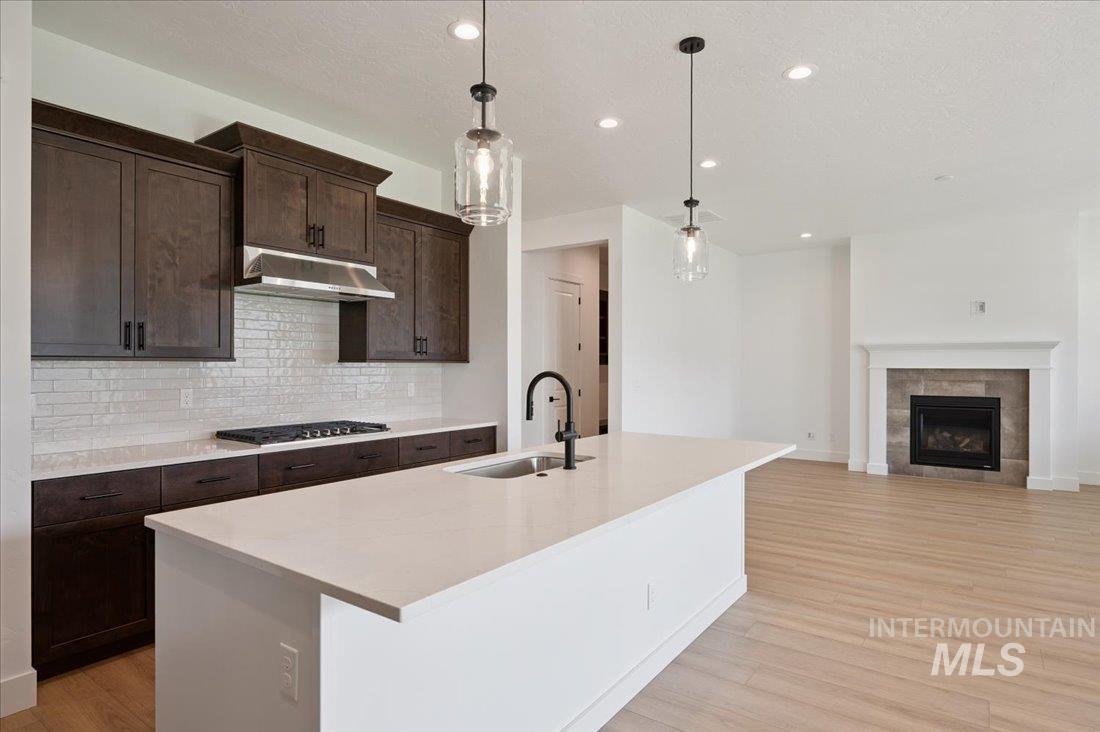Kitchen featuring pendant lighting, decorative backsplash, light wood finished floors, dark brown cabinets, and recessed lighting