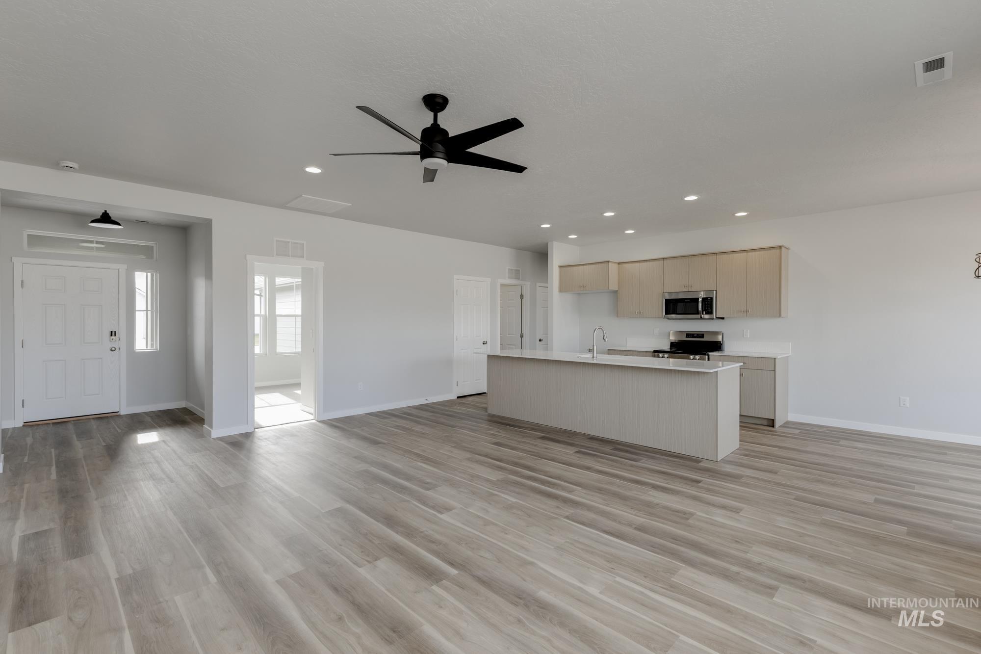 Kitchen featuring open floor plan, a ceiling fan, an island with sink, appliances with stainless steel finishes, and light wood finished floors