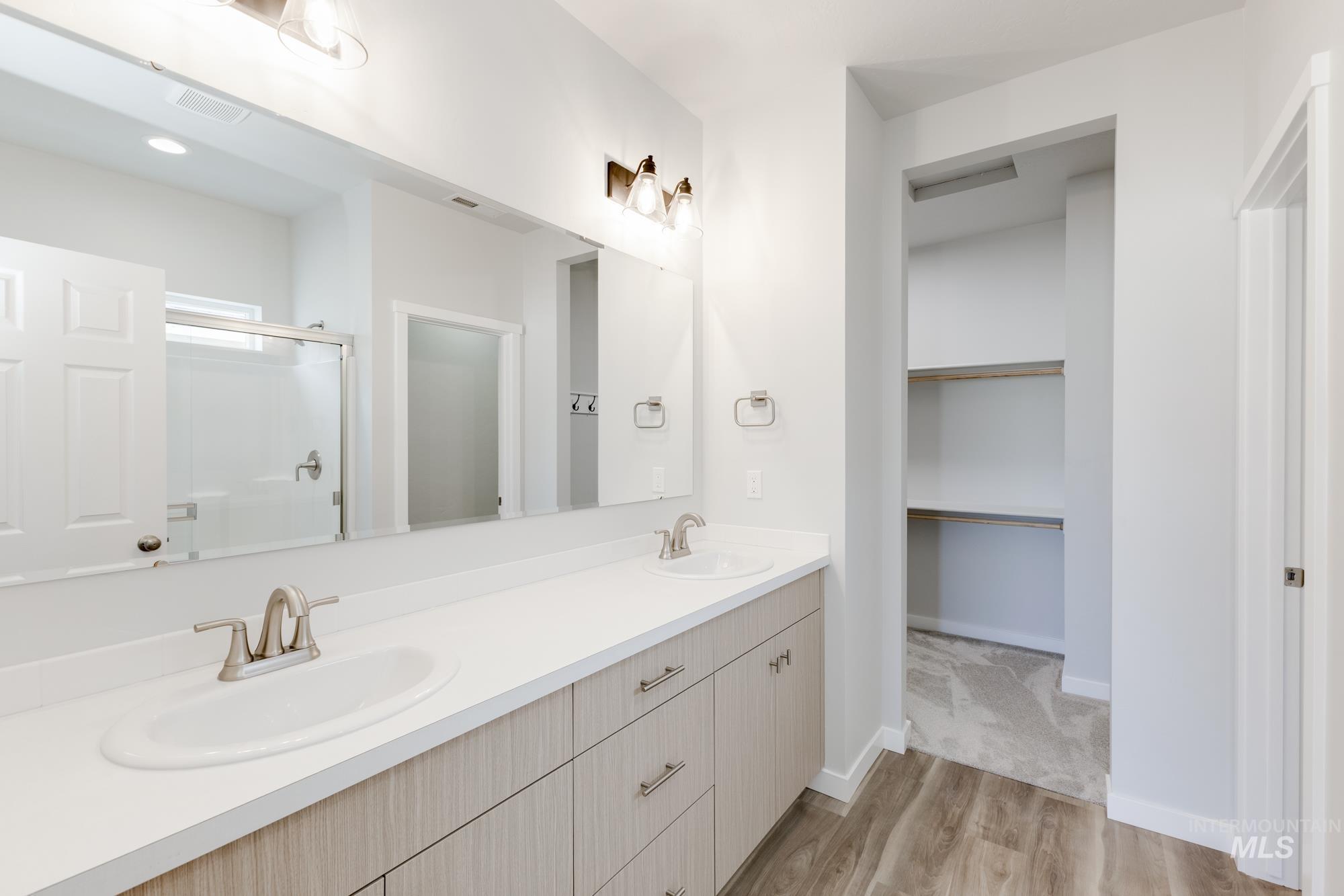 Bathroom with double vanity, a stall shower, light wood-style flooring, and a walk in closet