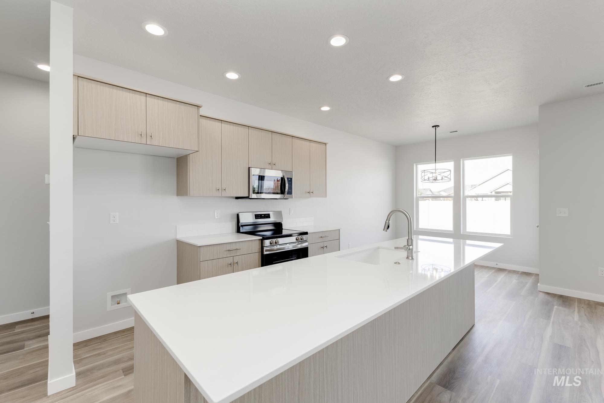 Kitchen featuring recessed lighting, appliances with stainless steel finishes, light wood-style floors, a kitchen island with sink, and pendant lighting