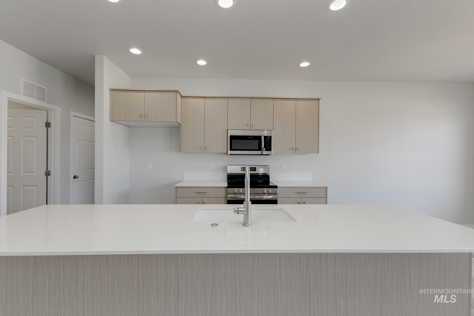 Kitchen featuring light brown cabinets, modern cabinets, an island with sink, light stone counters, and recessed lighting