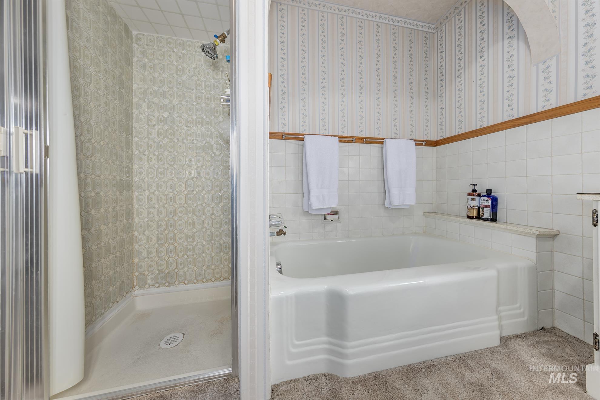 Full bath with tile walls, a shower stall, a bath, and wainscoting