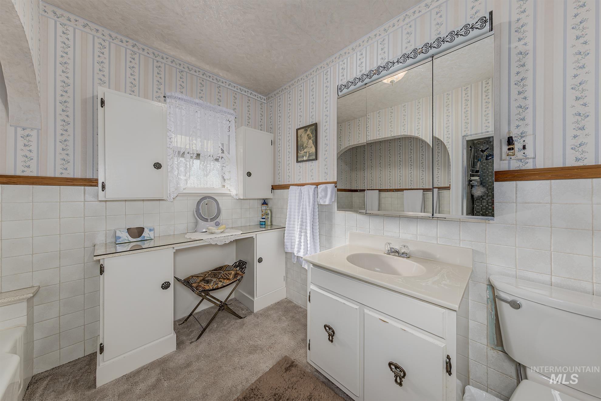 Full bathroom featuring tile walls, vanity, wainscoting, and wallpapered walls
