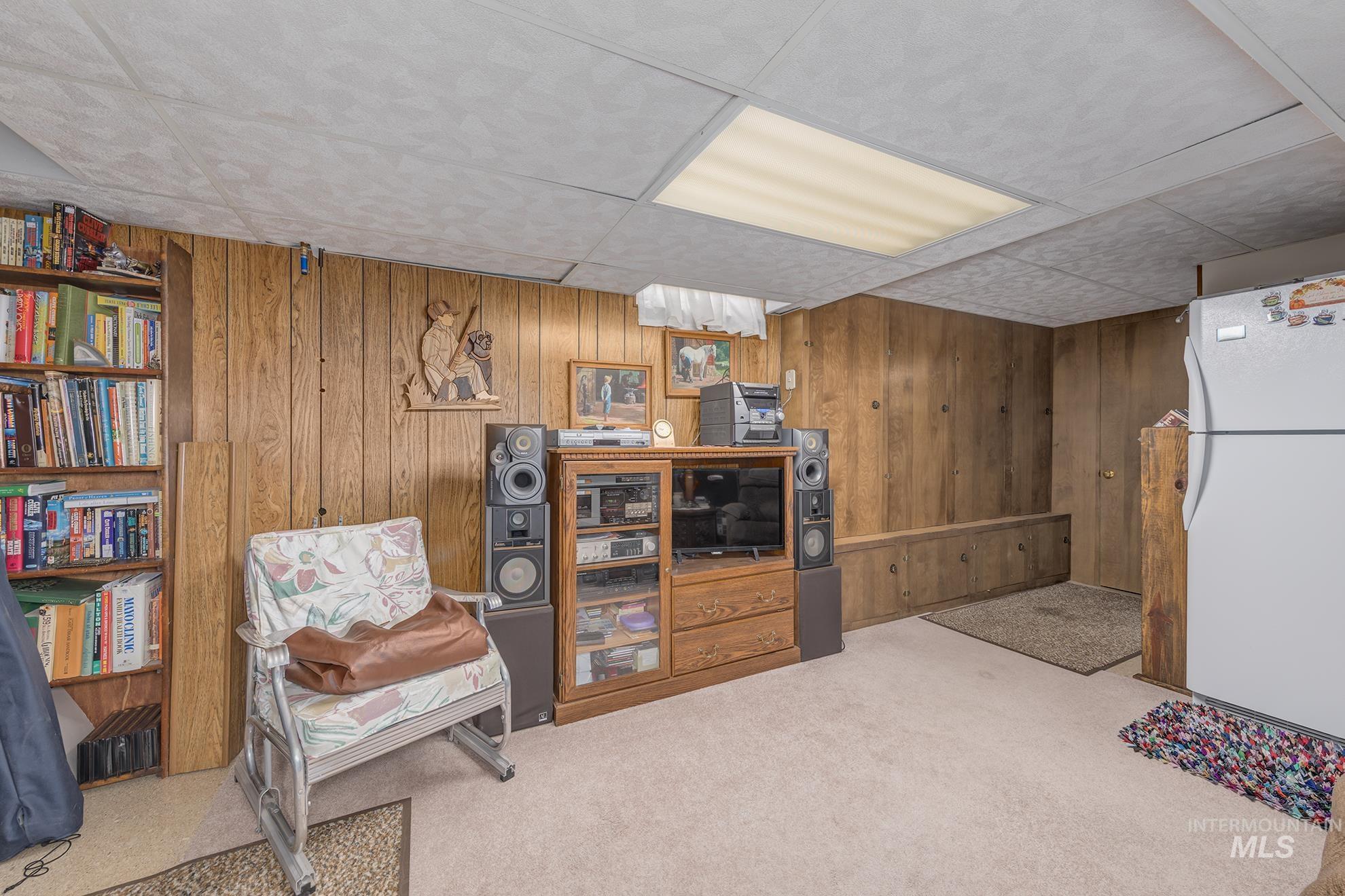 Sitting room featuring a drop ceiling, wooden walls, and light colored carpet