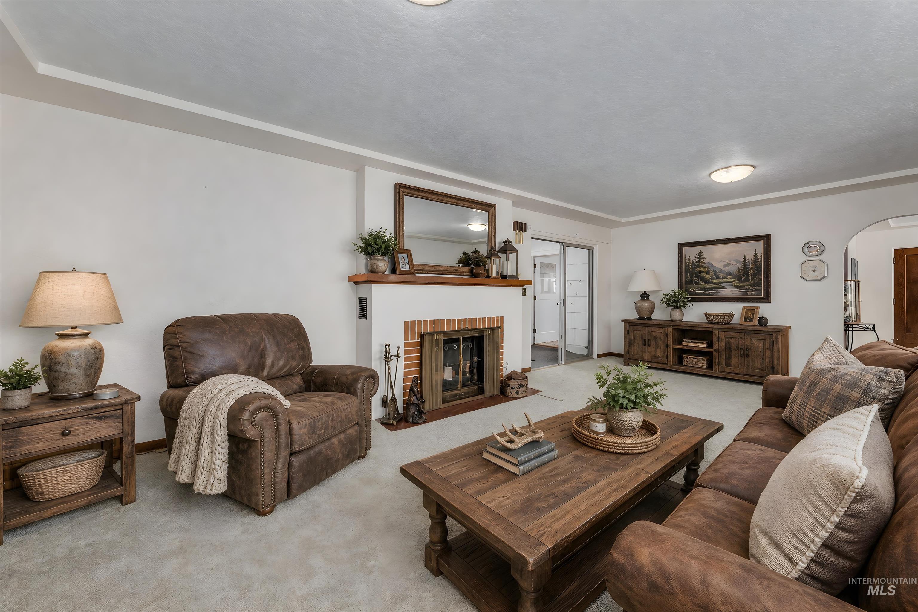 Living area featuring a white fireplace with a brick firebox and wood mantel, light-colored carpeting, white walls, and a coved ceiling