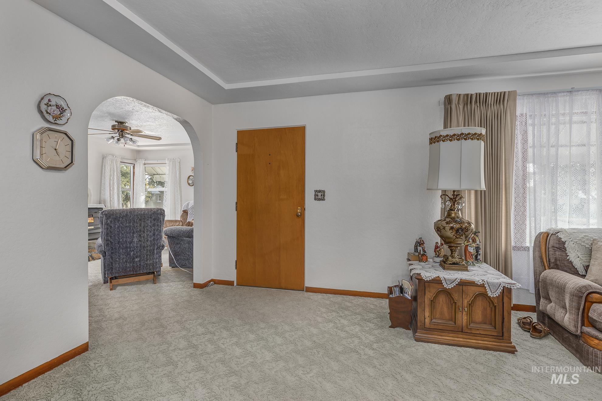 Living area featuring light colored carpet, arched walkways, a textured ceiling, a ceiling fan, and a tray ceiling