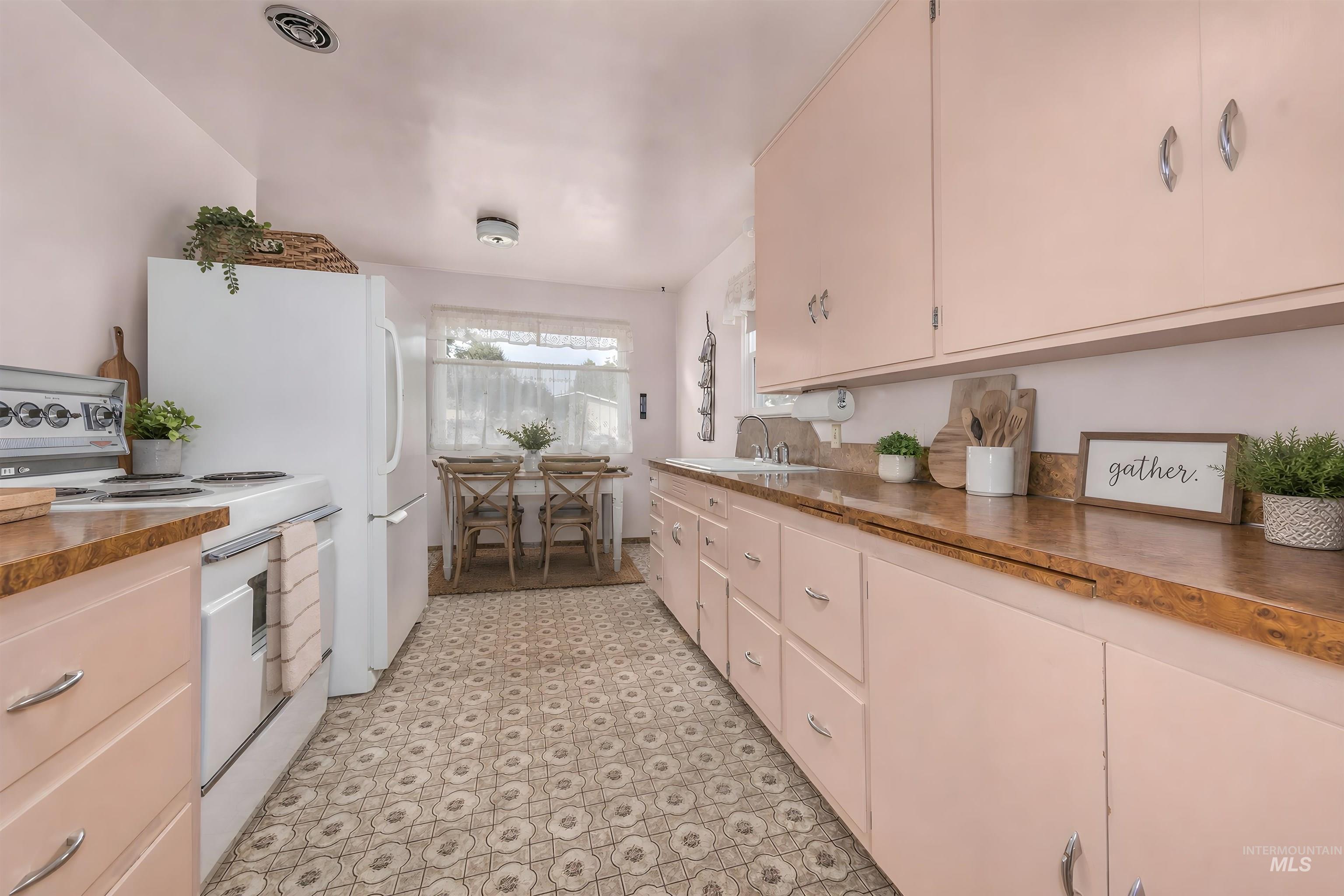 Kitchen featuring extensive pink cabinetry, patterned vinyl flooring, and a dining area with a window