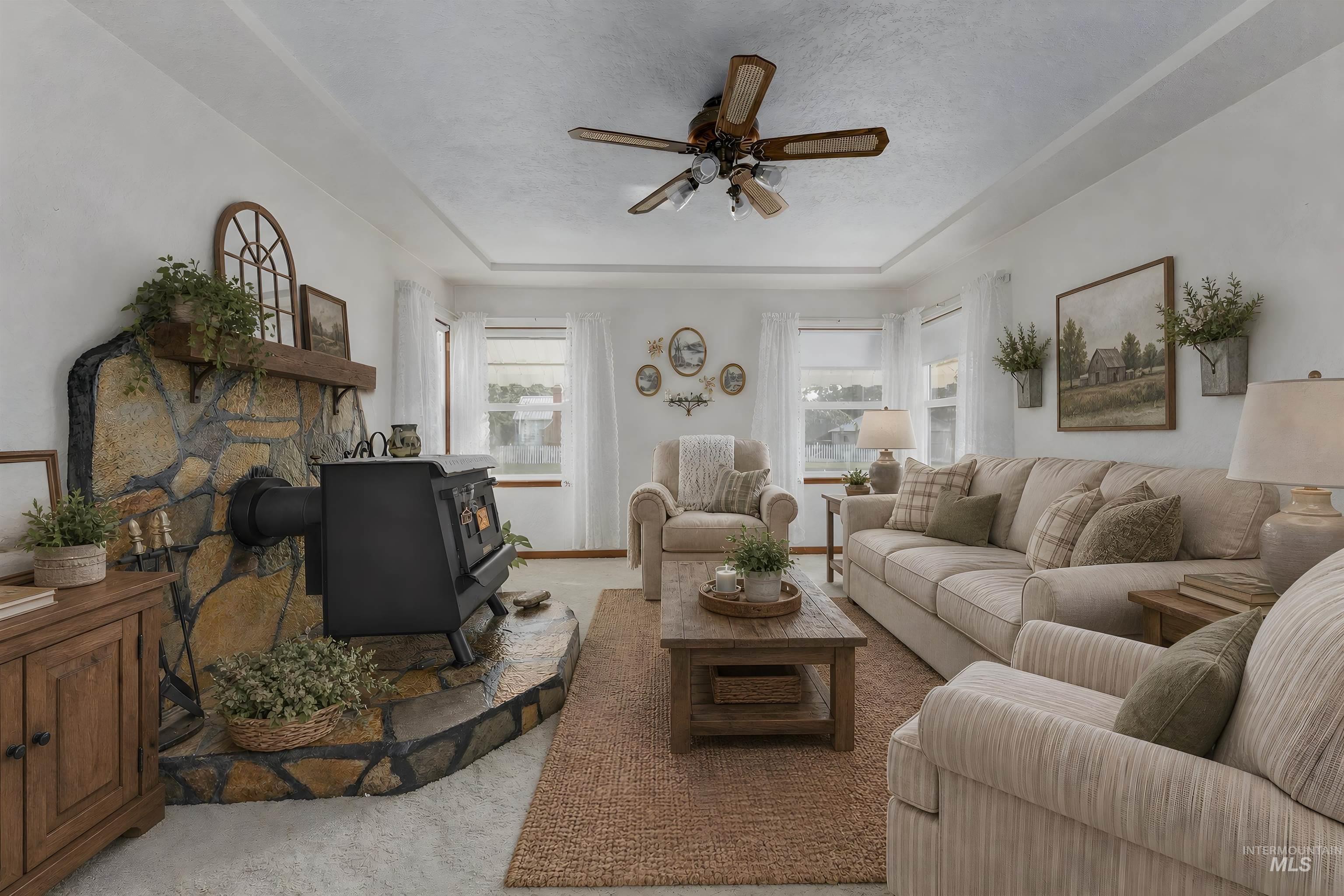 Living area featuring a stone wood-burning stove with mantel, tray ceiling, and ceiling fan
