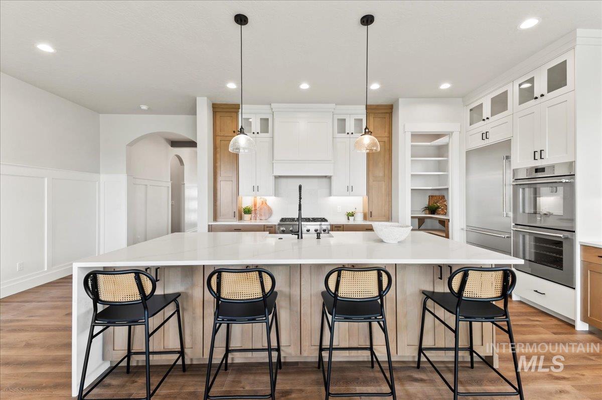 Kitchen with stainless steel appliances, light wood-style flooring, arched walkways, recessed lighting, and glass insert cabinets