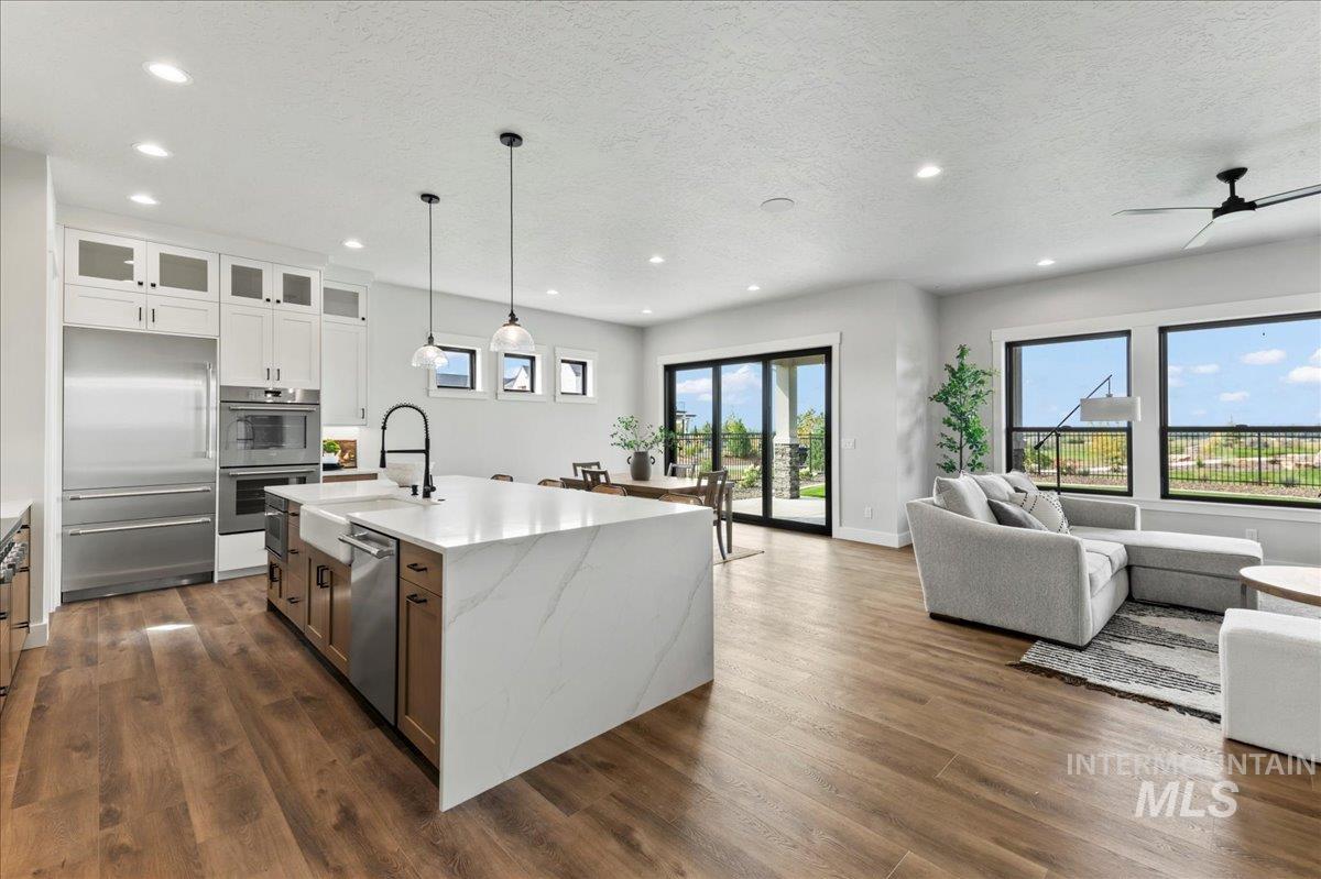 Kitchen with open floor plan, stainless steel appliances, light stone counters, white cabinetry, and pendant lighting