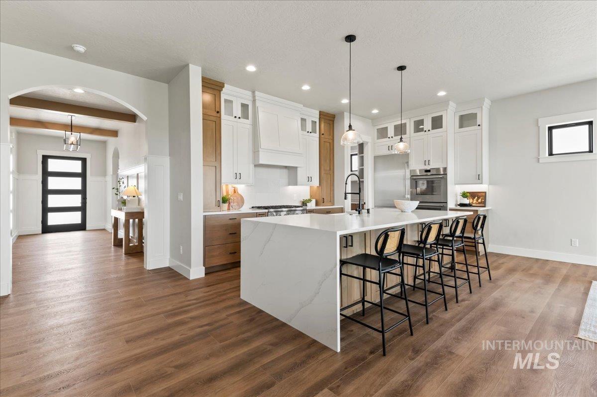 Kitchen featuring arched walkways, a breakfast bar area, beamed ceiling, a spacious island, and light stone counters