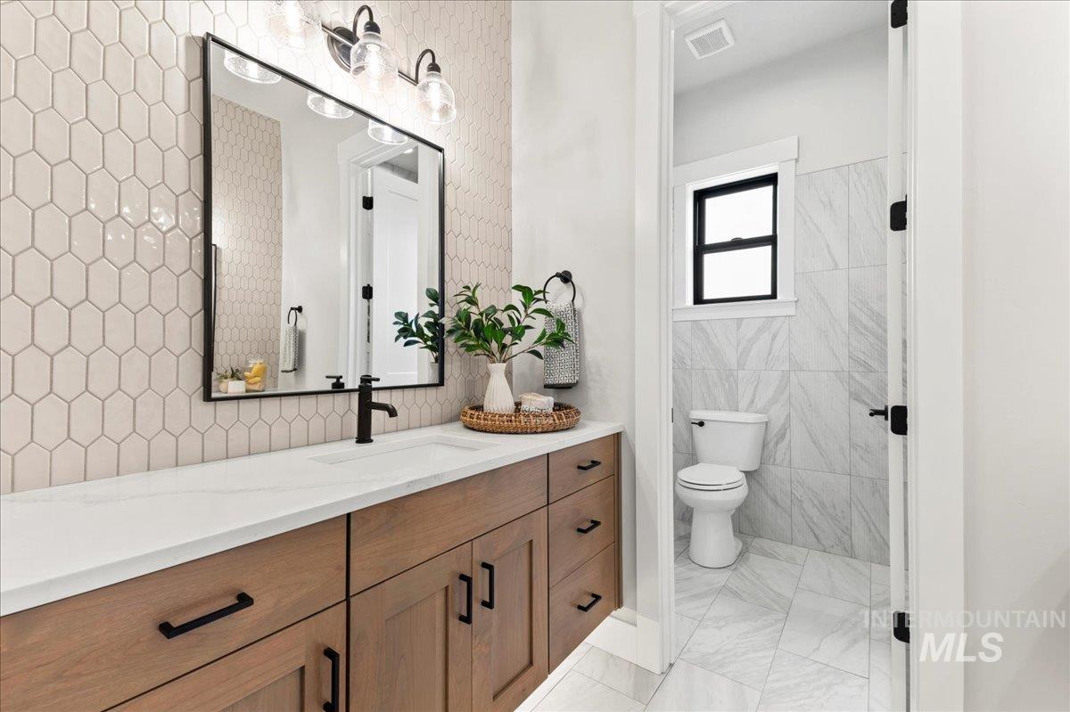 Full bath featuring vanity, light marble finish flooring, and tile walls