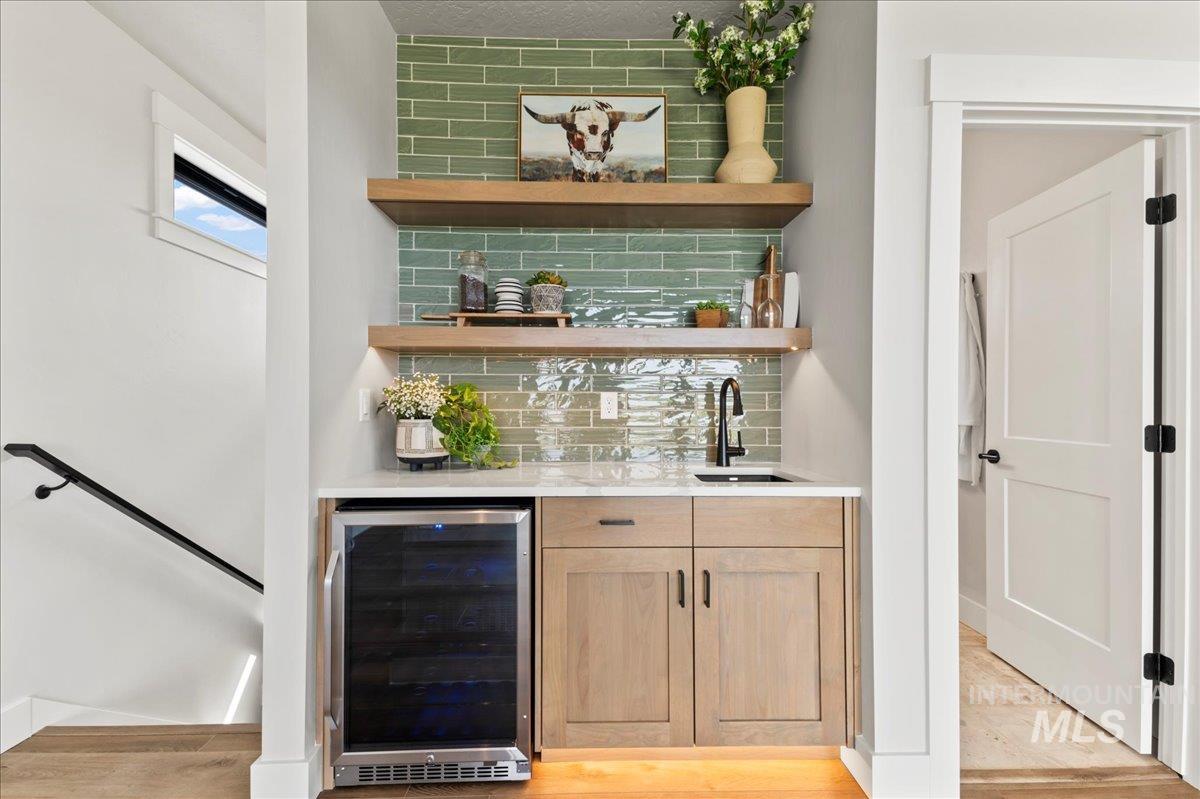 Indoor wet bar featuring tasteful backsplash, beverage cooler, open shelves, and light brown cabinets