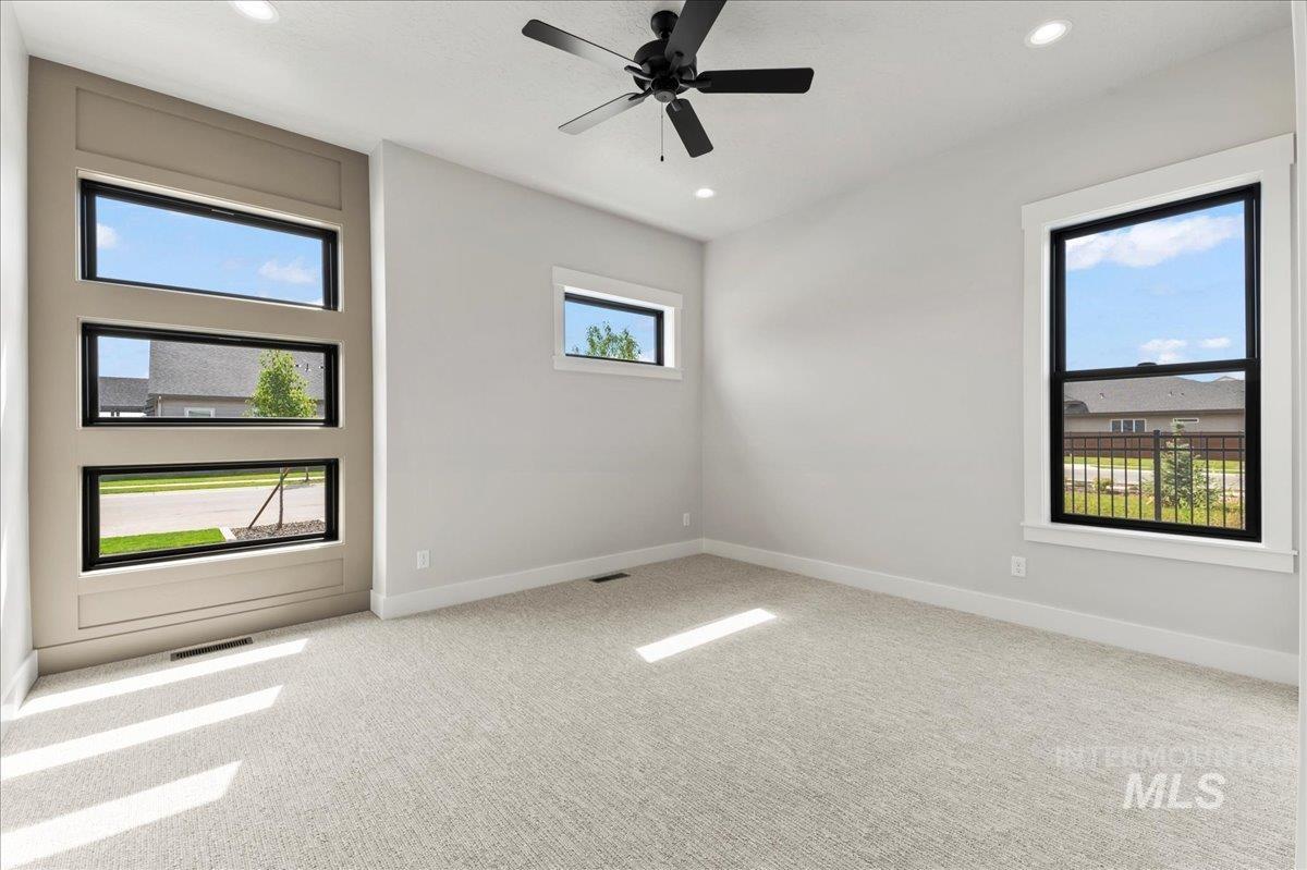 Empty room with light colored carpet, healthy amount of natural light, recessed lighting, and a ceiling fan