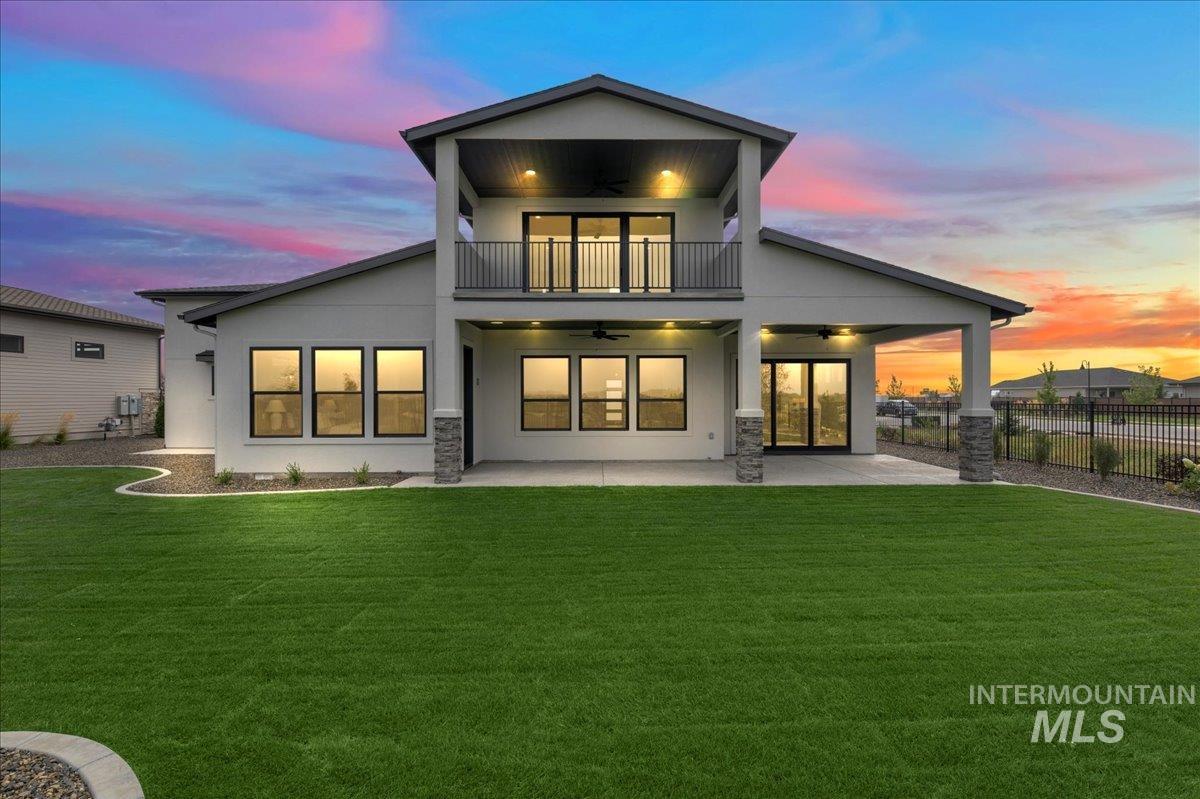 Back of property at dusk featuring ceiling fan, a patio area, stucco siding, and a balcony