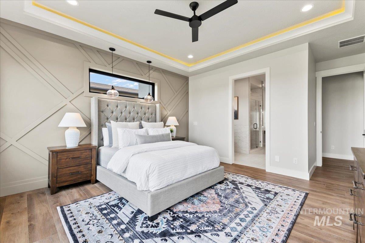 Bedroom featuring a raised ceiling, ceiling fan, light wood-style floors, recessed lighting, and a decorative wall
