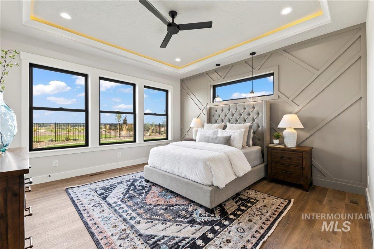 Bedroom with a raised ceiling, a ceiling fan, wood finished floors, recessed lighting, and a decorative wall