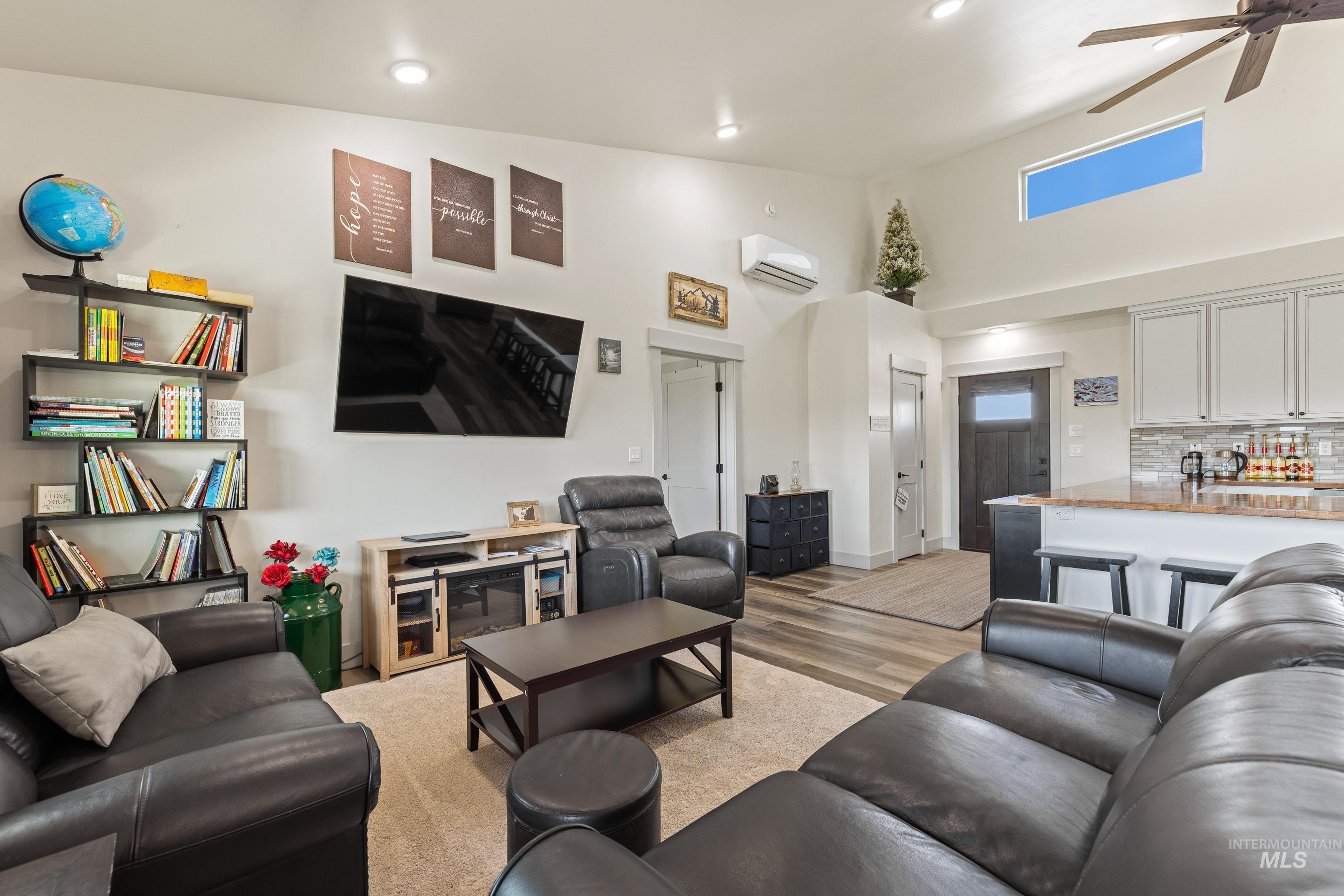 Living area with ceiling fan, light wood-style floors, a wall mounted air conditioner, recessed lighting, and a high ceiling