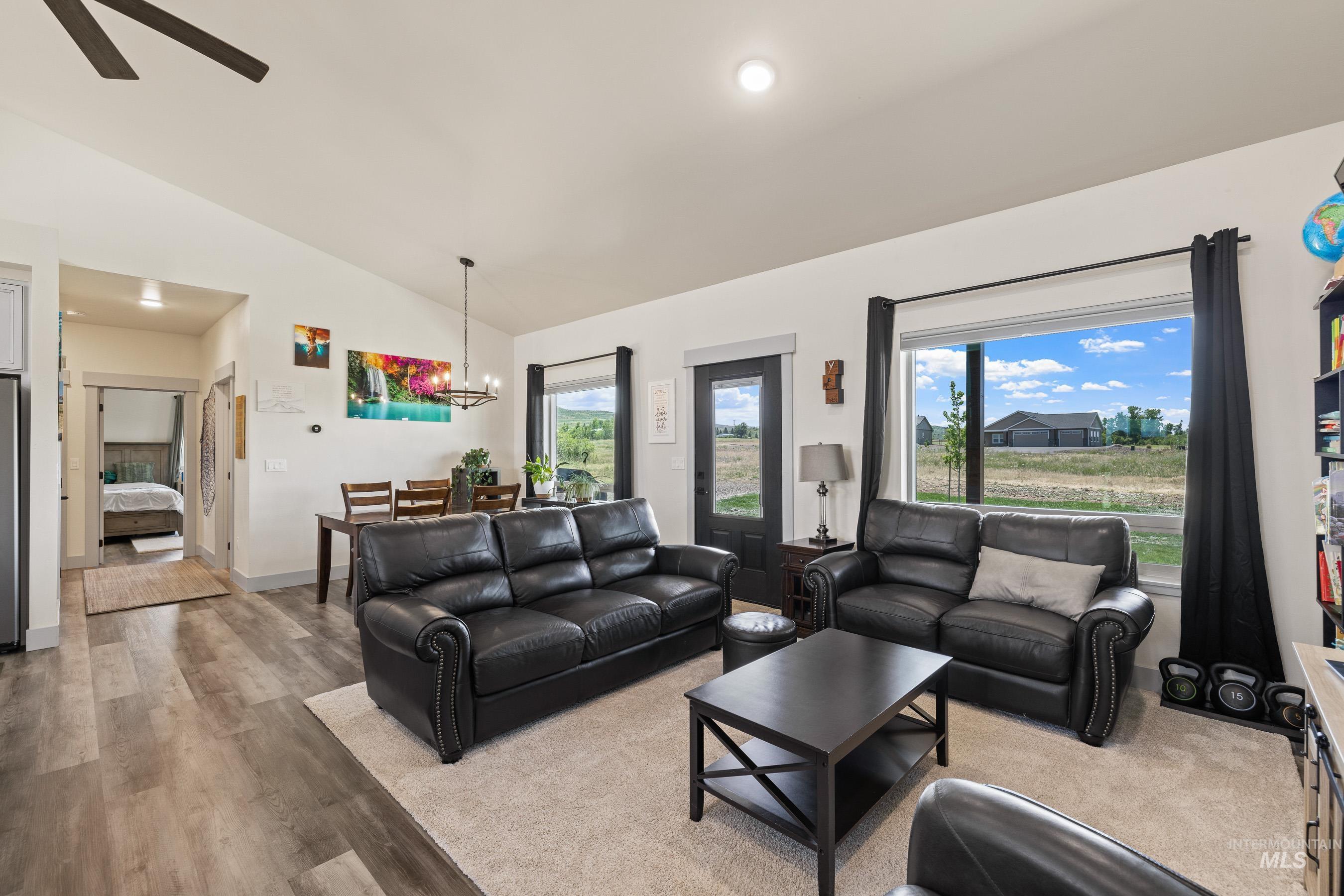 Living room featuring vaulted ceiling, light wood-style flooring, a ceiling fan, and a chandelier