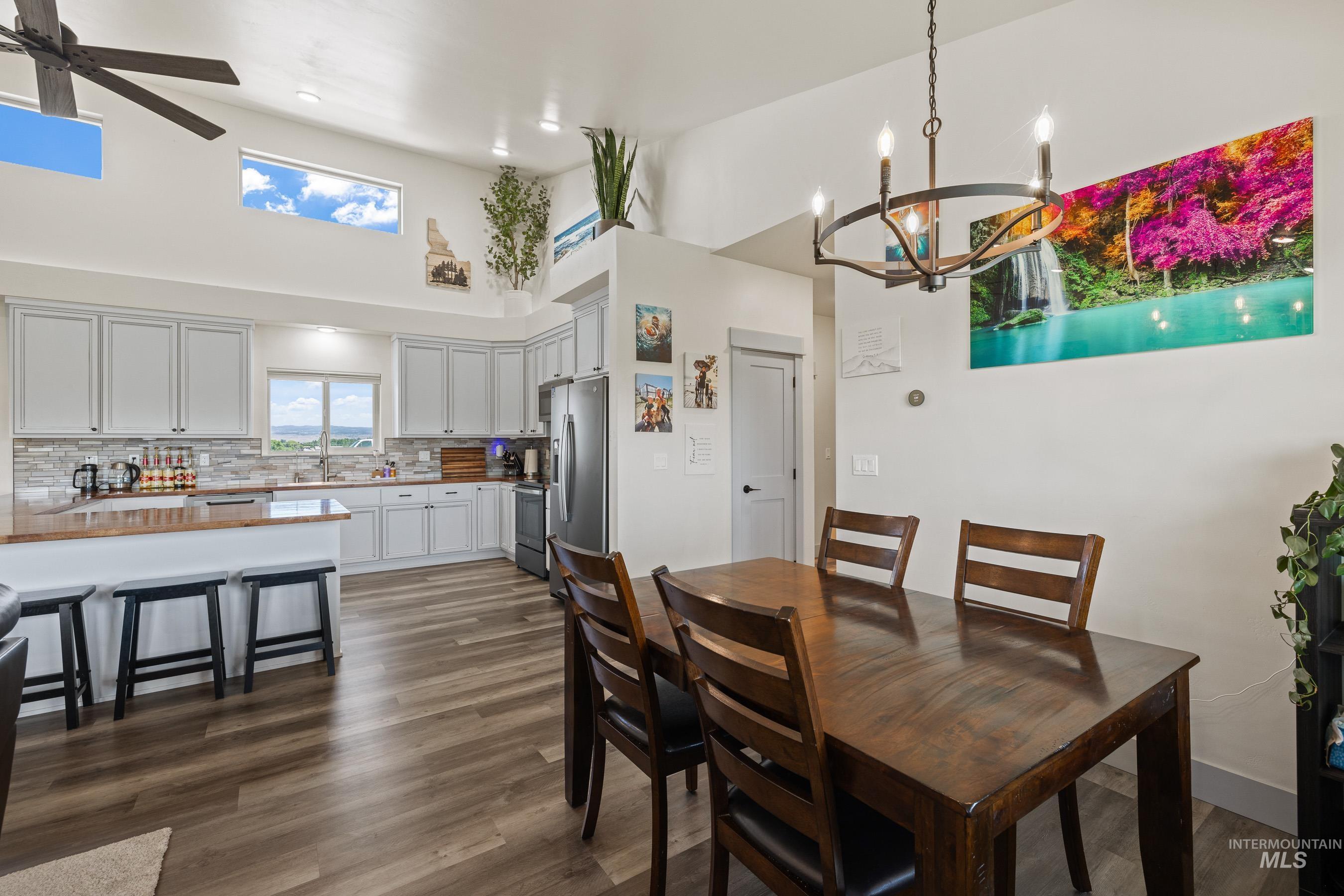 Dining space with a towering ceiling, a chandelier, ceiling fan, and dark wood-style floors