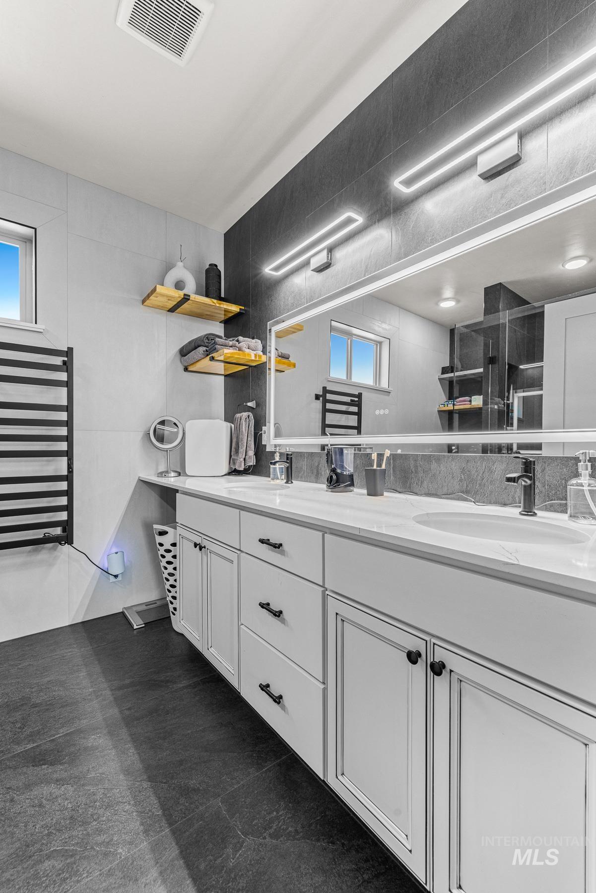 Full bath featuring double vanity, healthy amount of natural light, and an enclosed shower