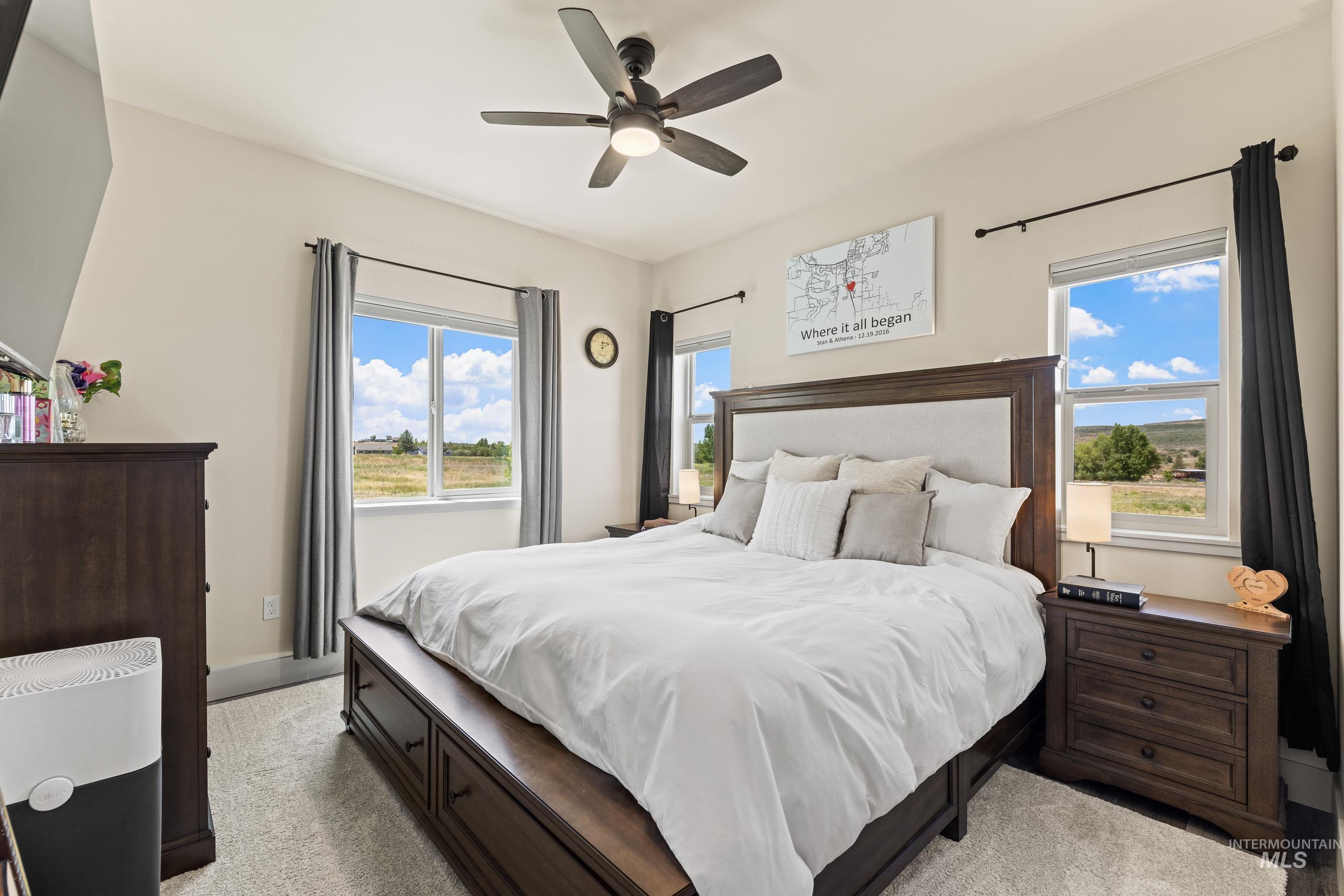 Bedroom with light colored carpet, multiple windows, and a ceiling fan
