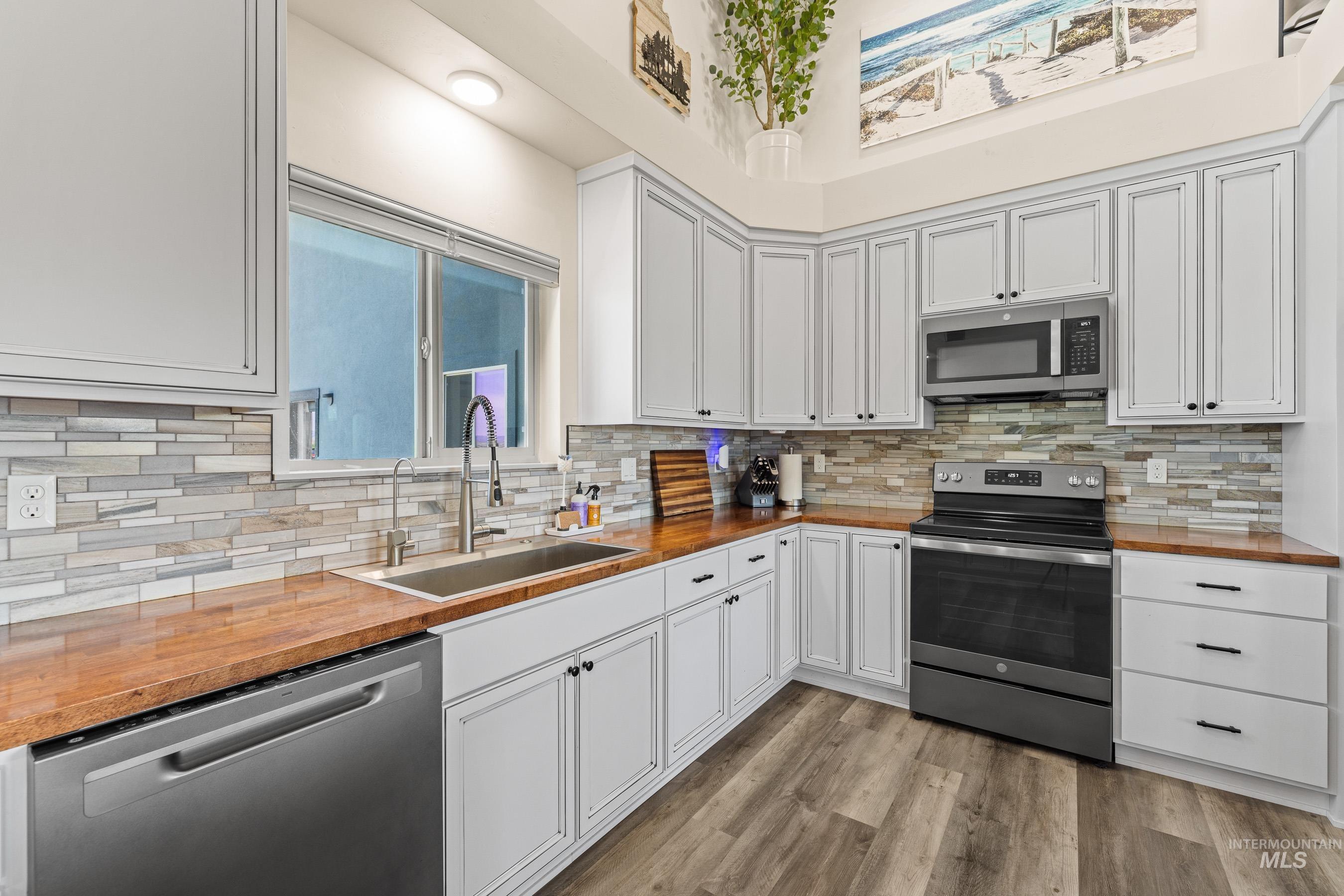 Kitchen with appliances with stainless steel finishes, butcher block counters, tasteful backsplash, and light wood-type flooring