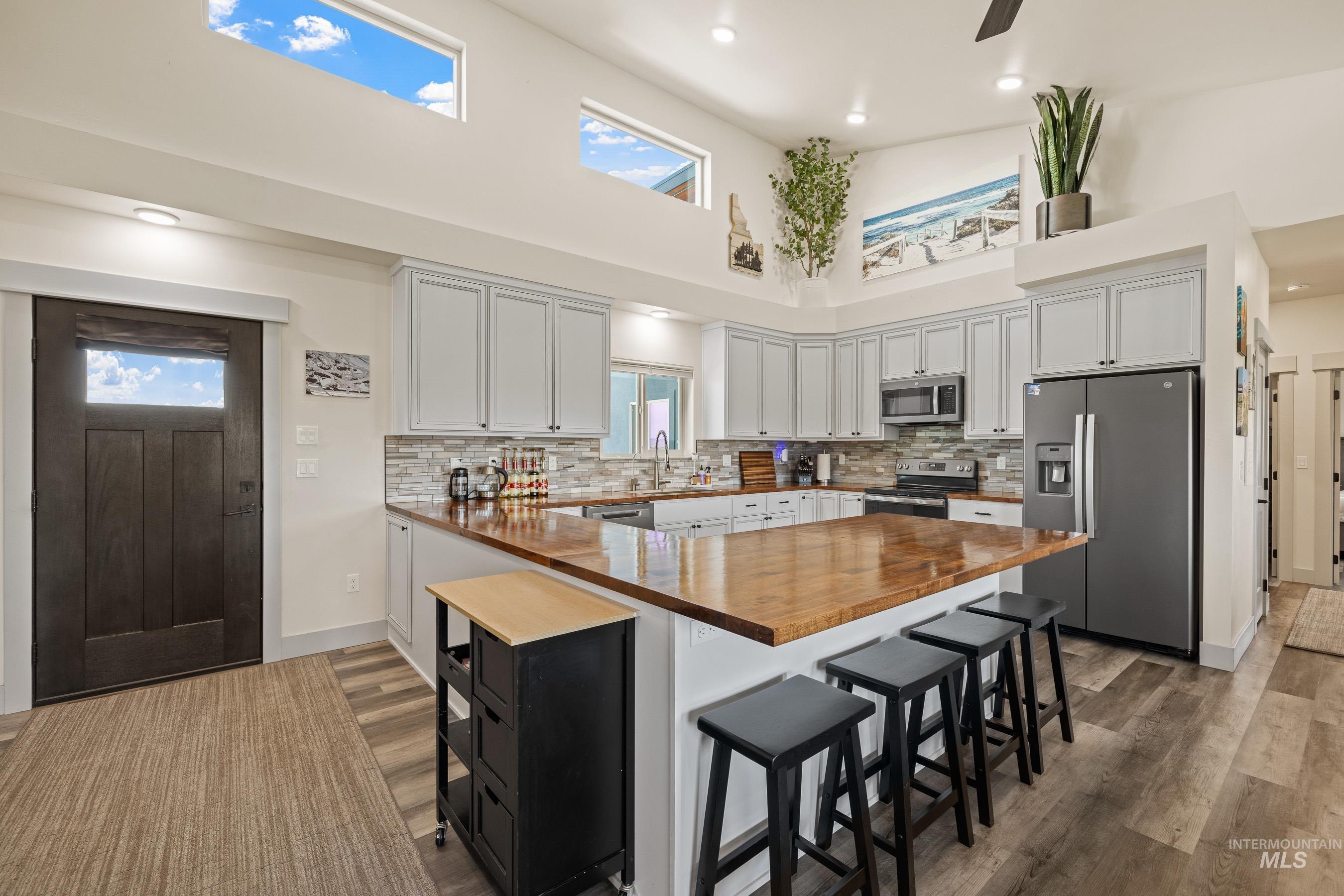 Kitchen featuring stainless steel appliances, wood counters, a towering ceiling, a breakfast bar, and tasteful backsplash