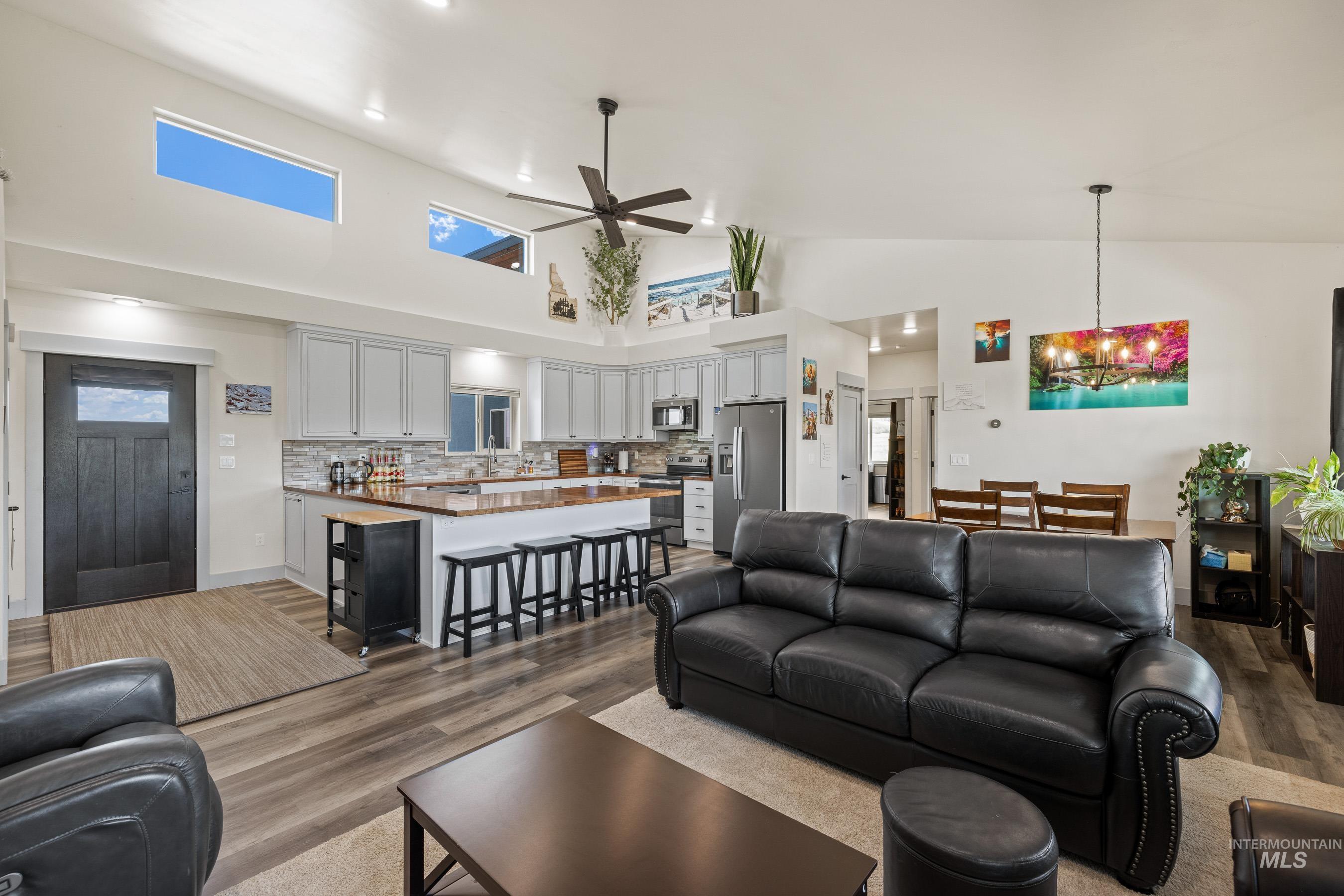Living room featuring wood finished floors, ceiling fan, a chandelier, high vaulted ceiling, and recessed lighting