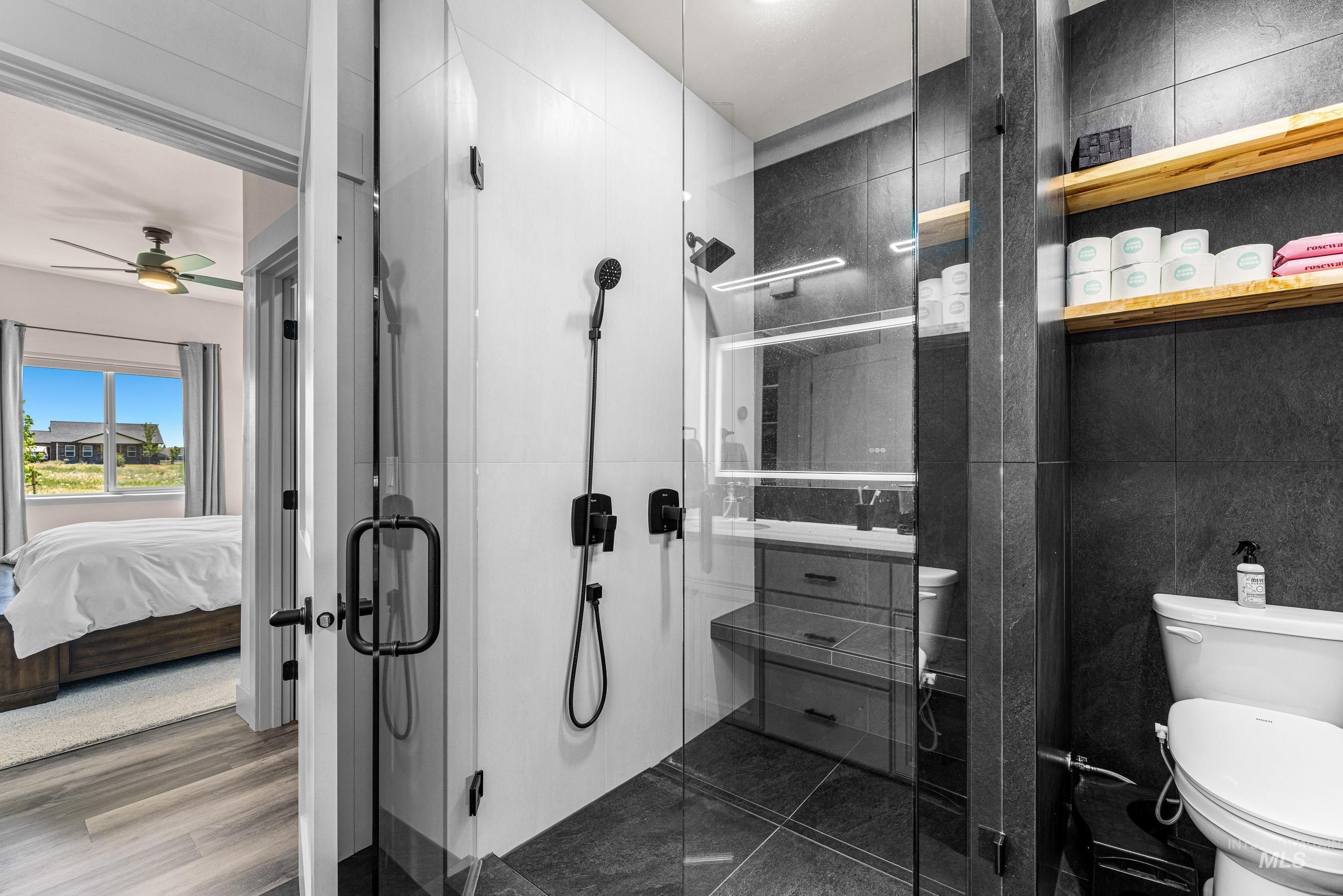 Full bath featuring a stall shower, a ceiling fan, ensuite bath, and tile walls