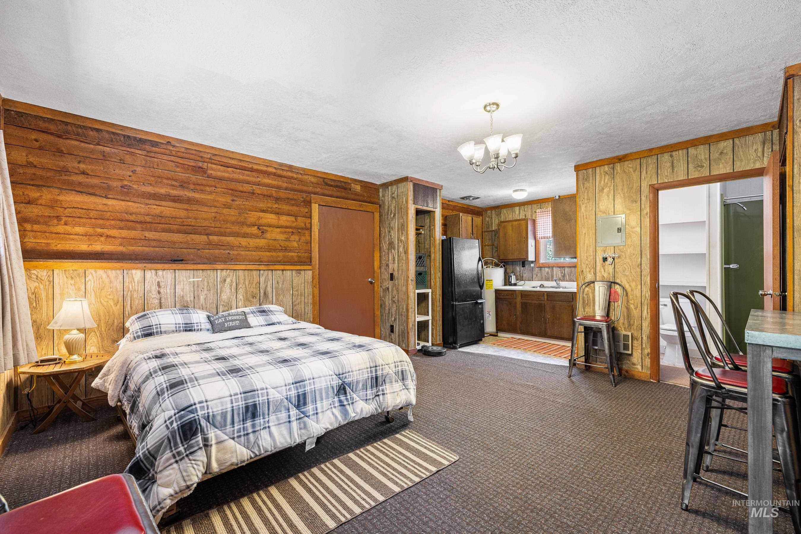 Bedroom featuring wood walls, dark colored carpet, freestanding refrigerator, a chandelier, and a textured ceiling