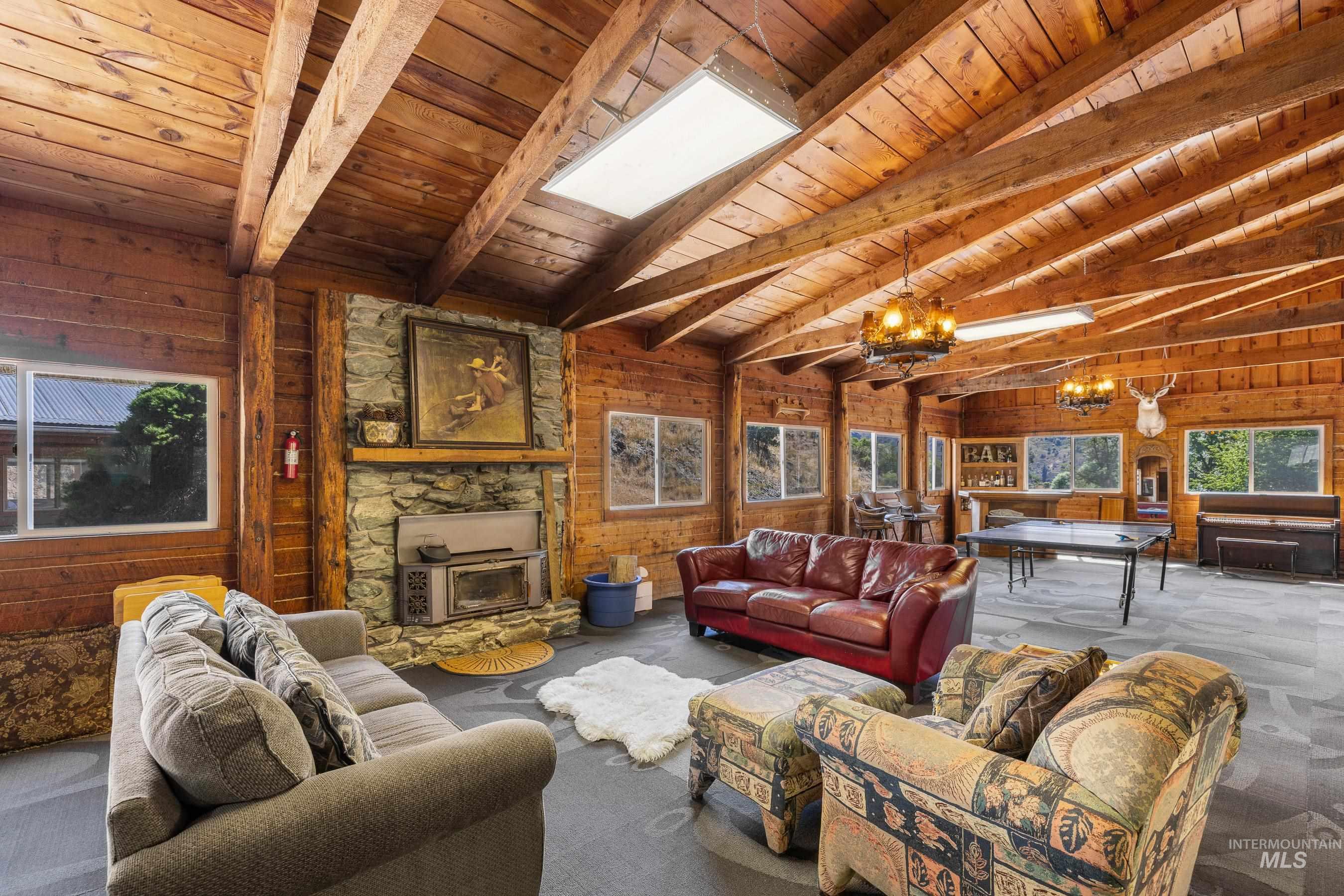 Living room featuring a chandelier, wood walls, a wood stove, carpet, and wooden ceiling