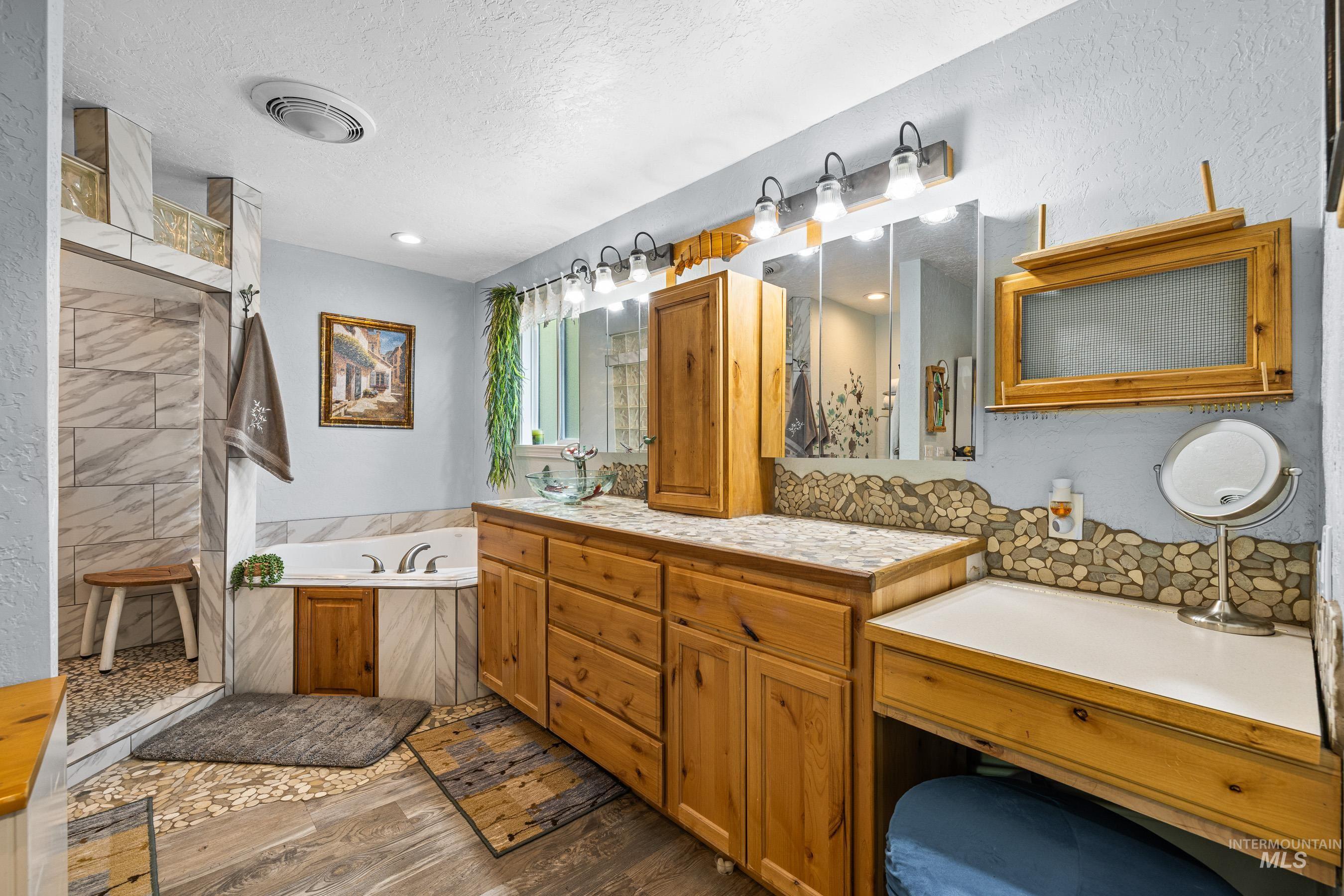 Full bath featuring a bath, double vanity, a textured ceiling, dark wood-style flooring, and tiled shower