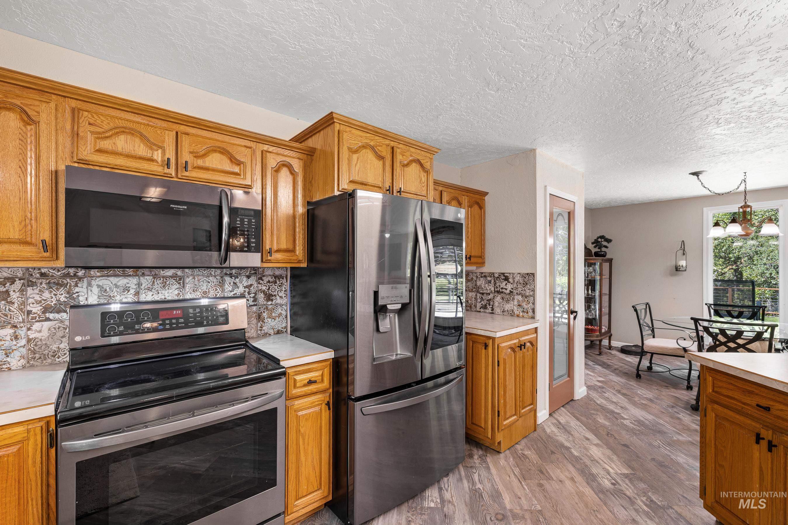 Kitchen featuring stainless steel appliances, light countertops, decorative backsplash, brown cabinets, and light wood finished floors