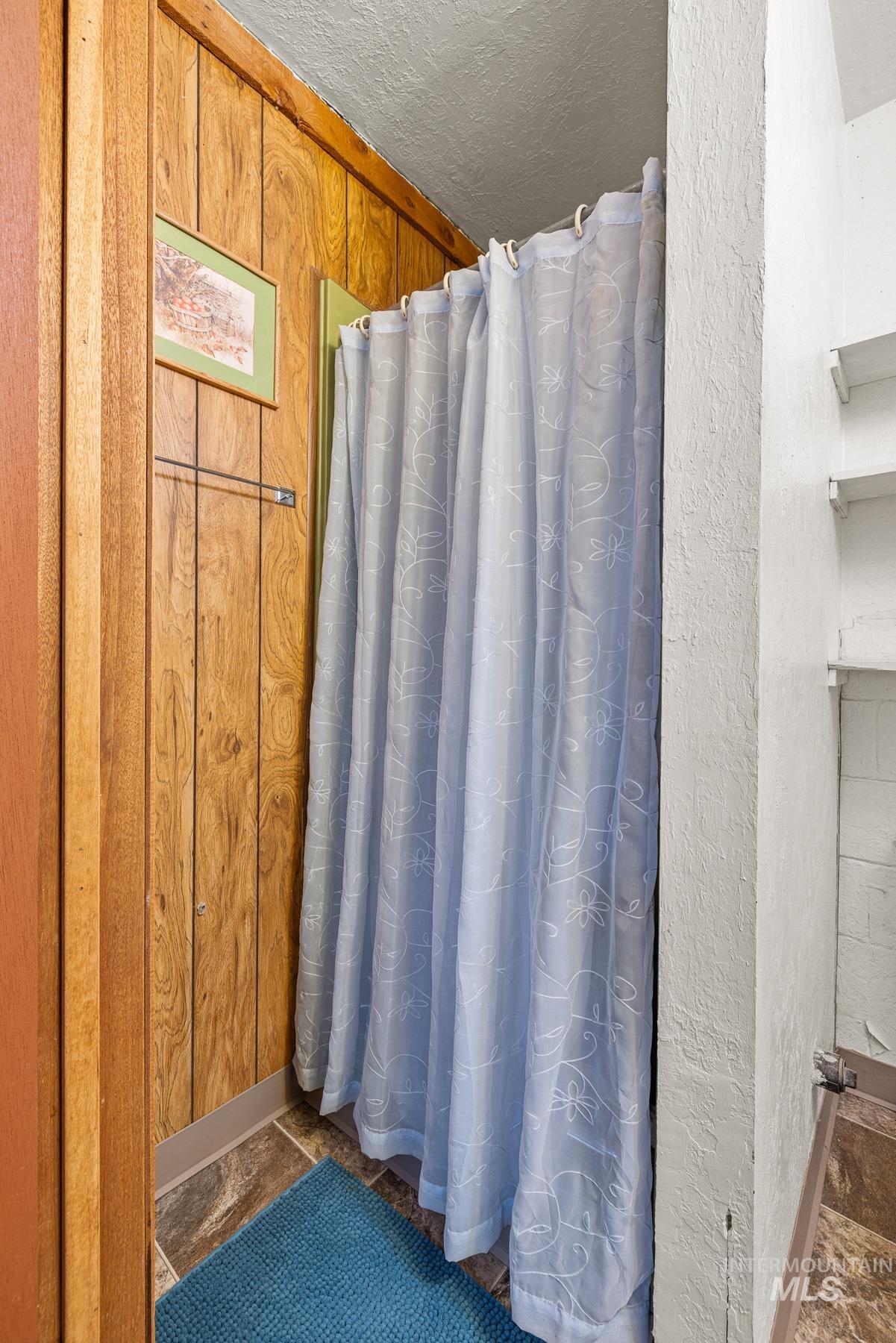 Full bath with a shower with curtain, a textured ceiling, a textured wall, and dark stone finish flooring