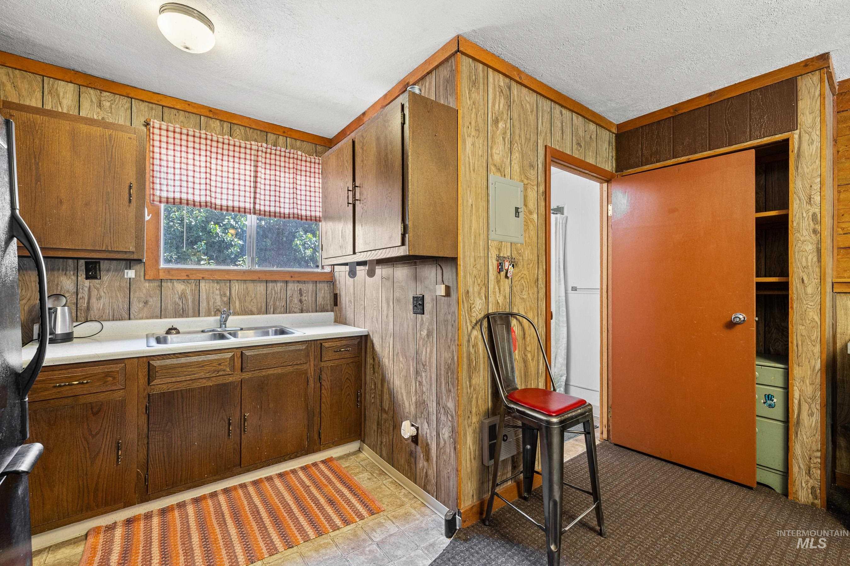 Bathroom with wooden walls, a textured ceiling, electric panel, and a garden tub