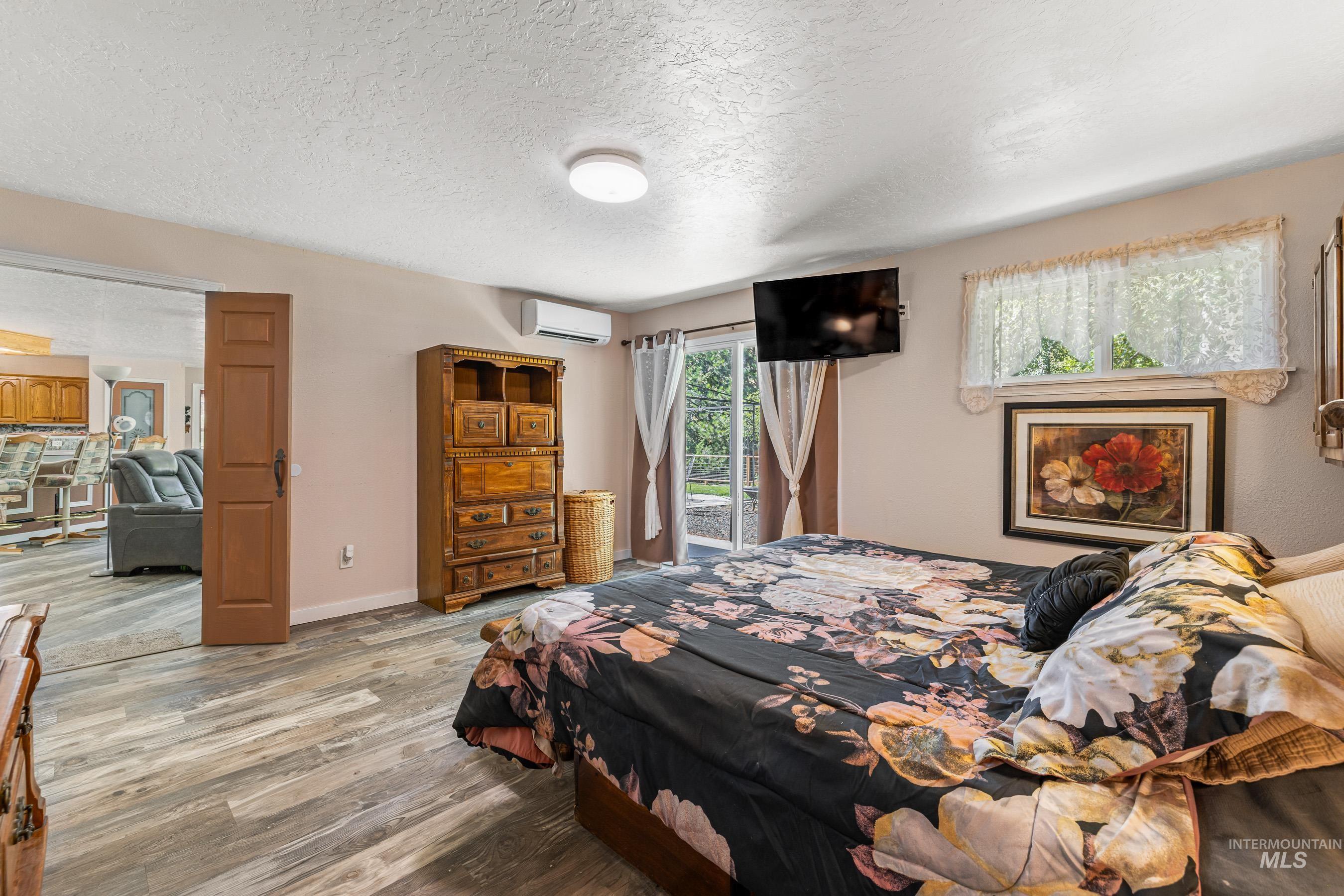Bedroom featuring access to outside, wood finished floors, a textured ceiling, and an AC wall unit