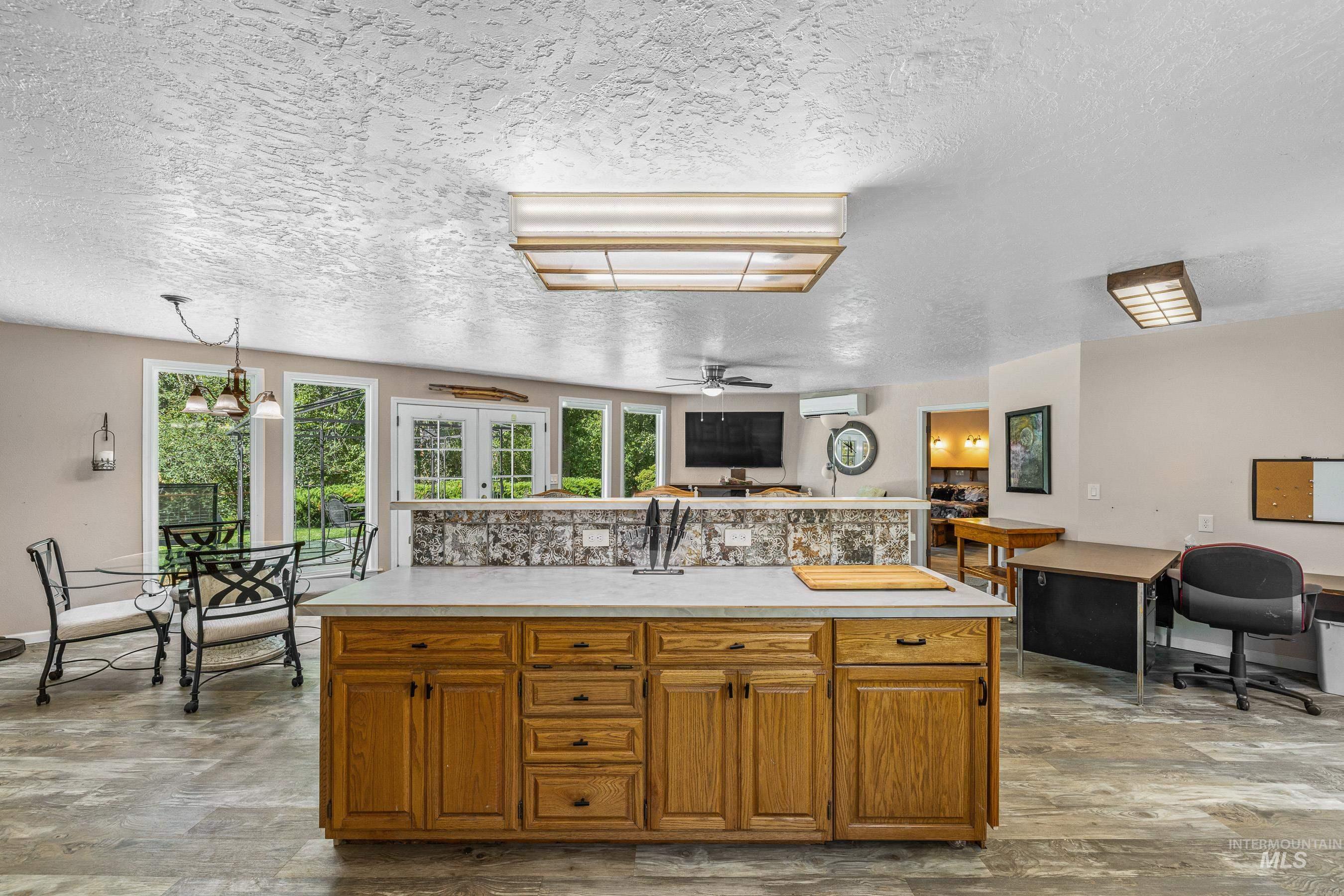 Kitchen featuring brown cabinetry, light countertops, a textured ceiling, a kitchen island, and decorative light fixtures