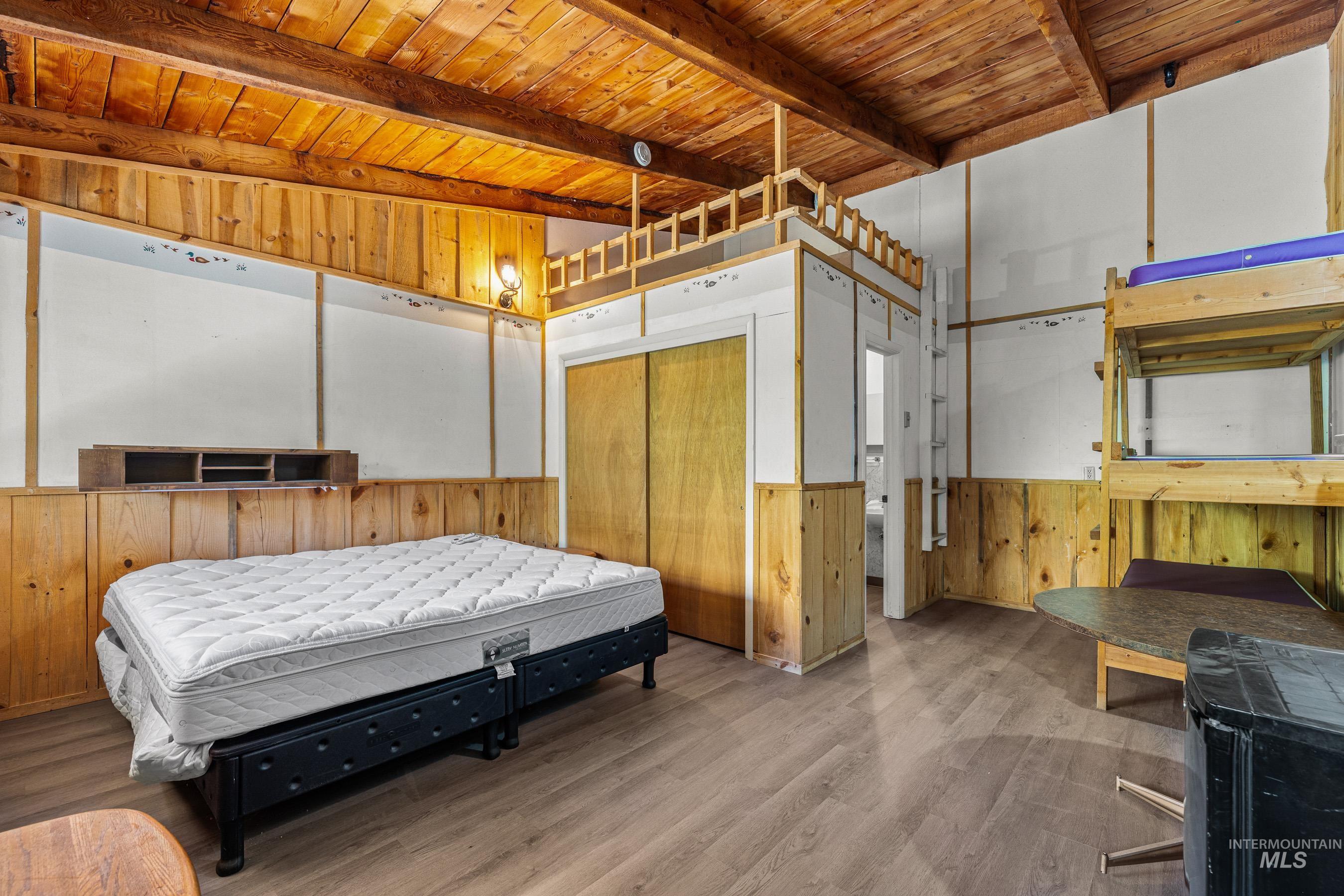 Bedroom featuring wooden walls, wainscoting, a wooden ceiling with exposed beams, and wood finished floors