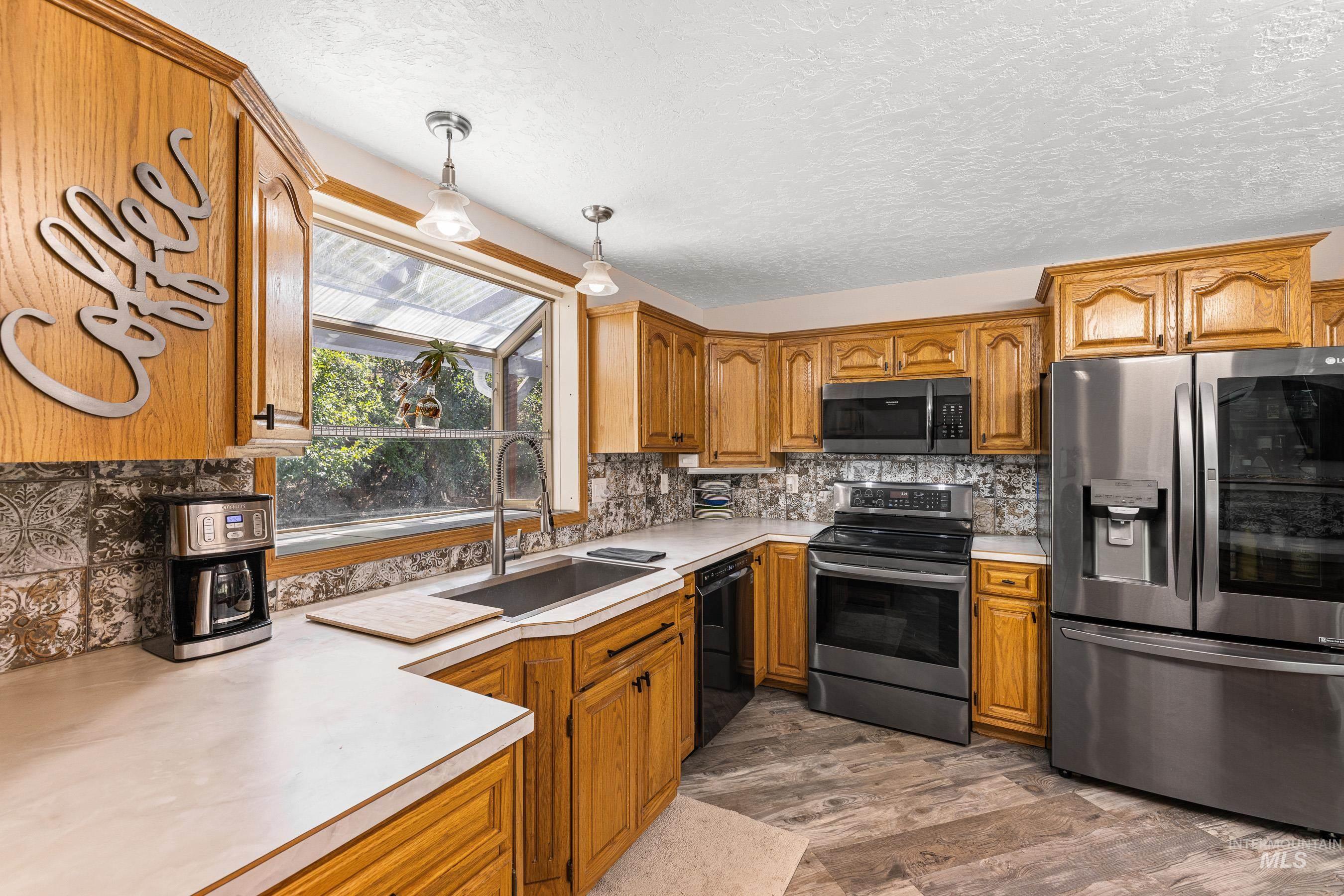 Kitchen with appliances with stainless steel finishes, light countertops, brown cabinetry, decorative backsplash, and a textured ceiling