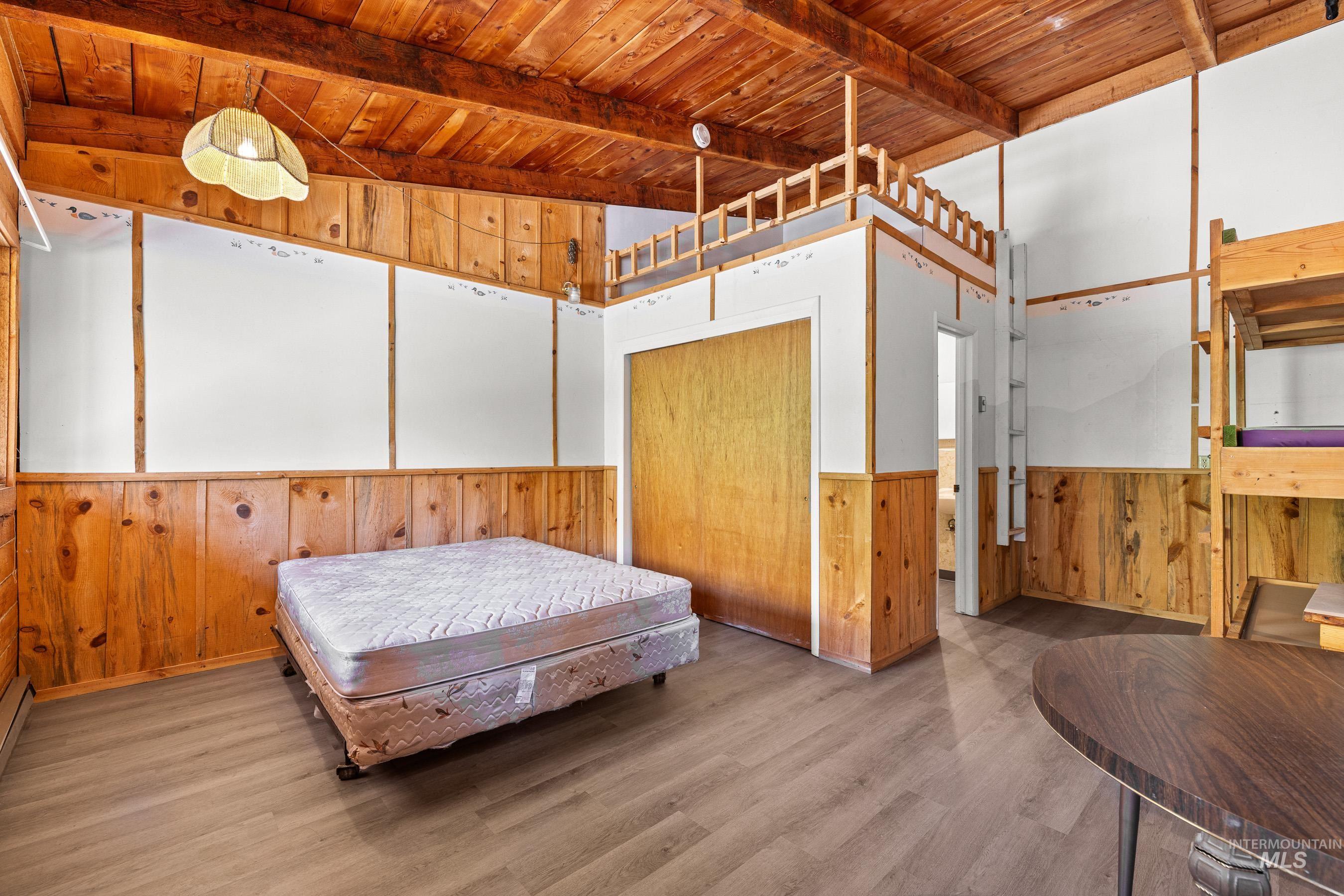 Bedroom with wooden walls, a wood ceiling with exposed beams, wood finished floors, and wainscoting