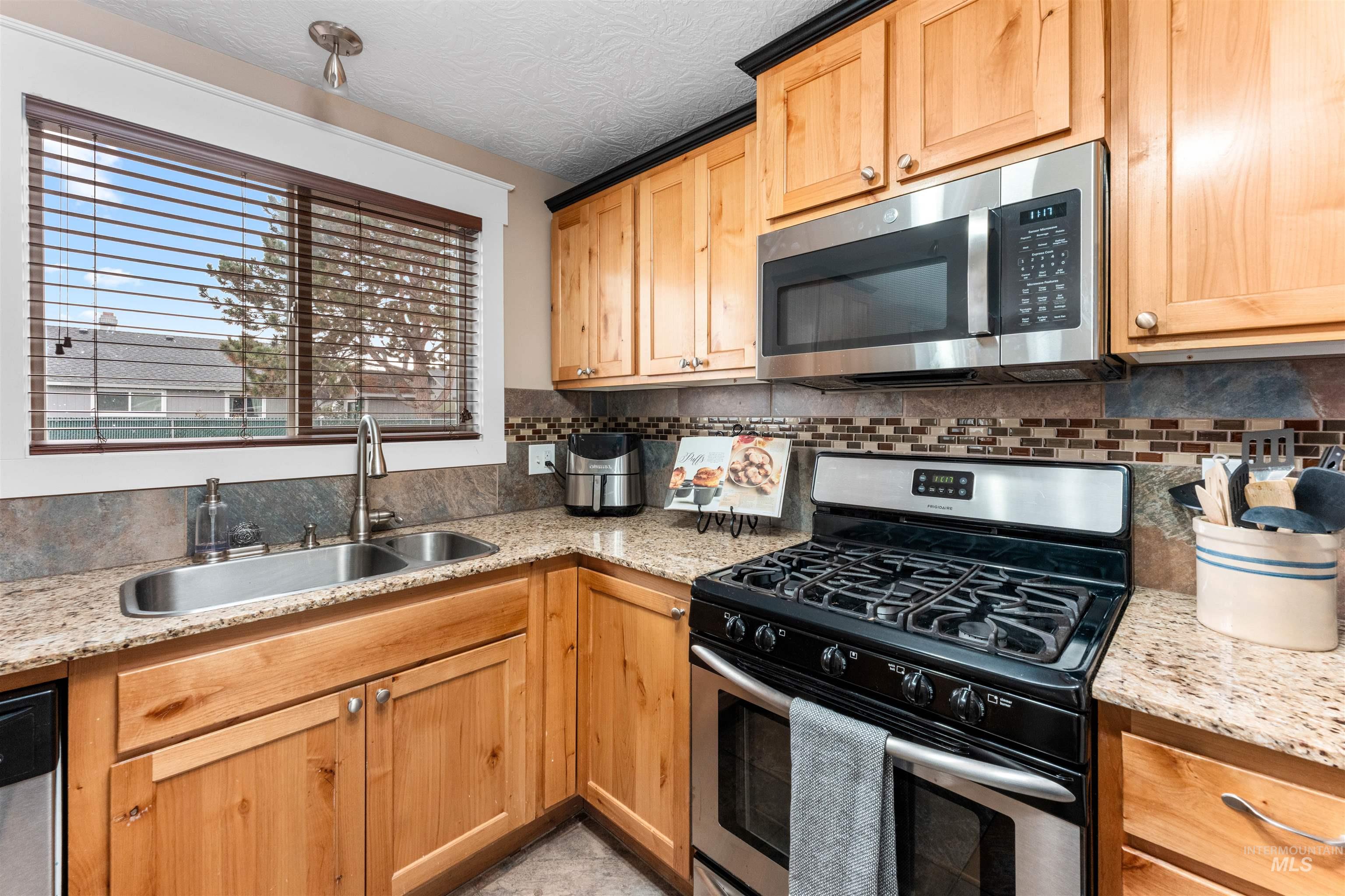 Kitchen featuring stainless steel appliances, light stone counters, and decorative backsplash