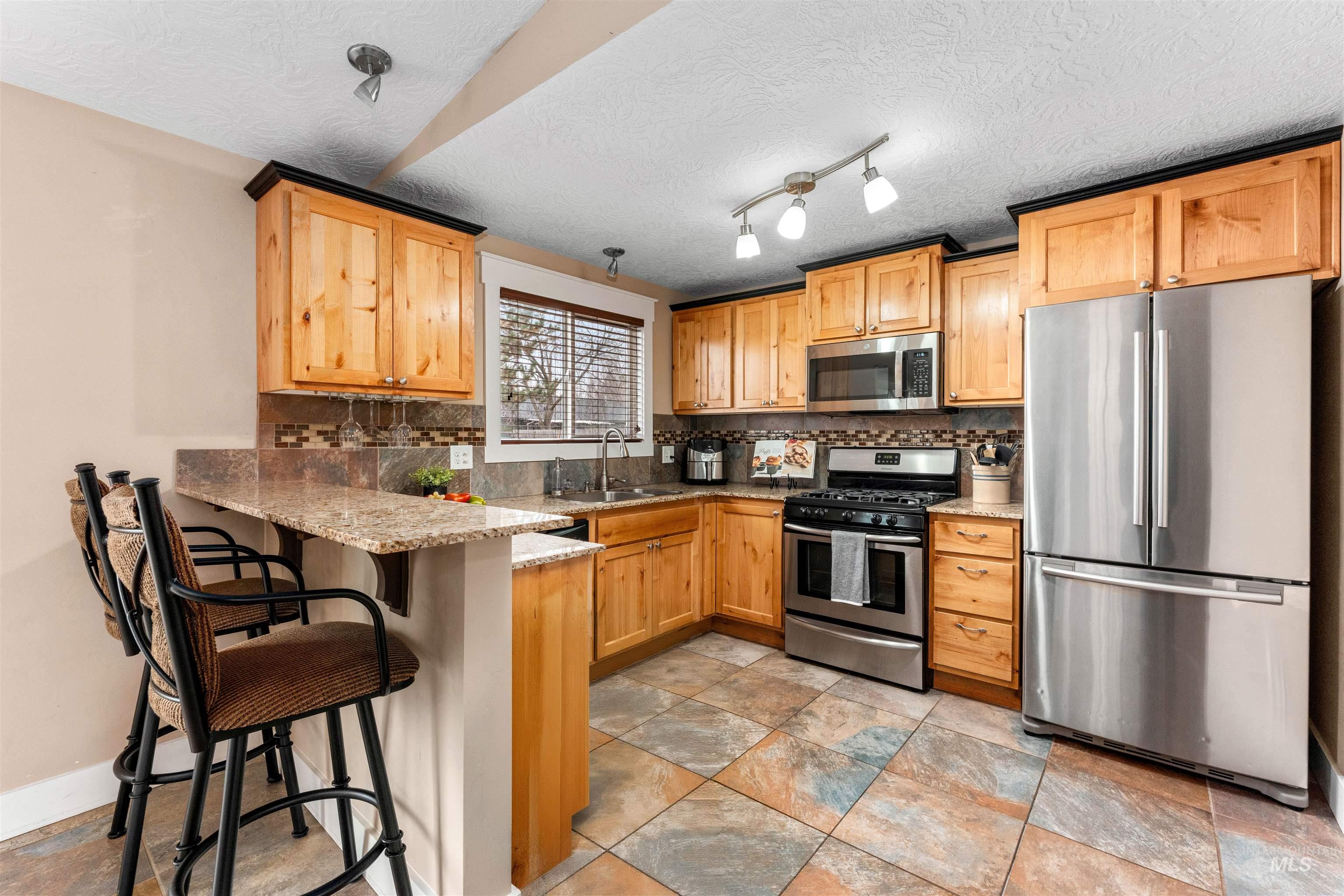 Kitchen featuring stainless steel appliances, a breakfast bar area, a peninsula, light stone counters, and tasteful backsplash