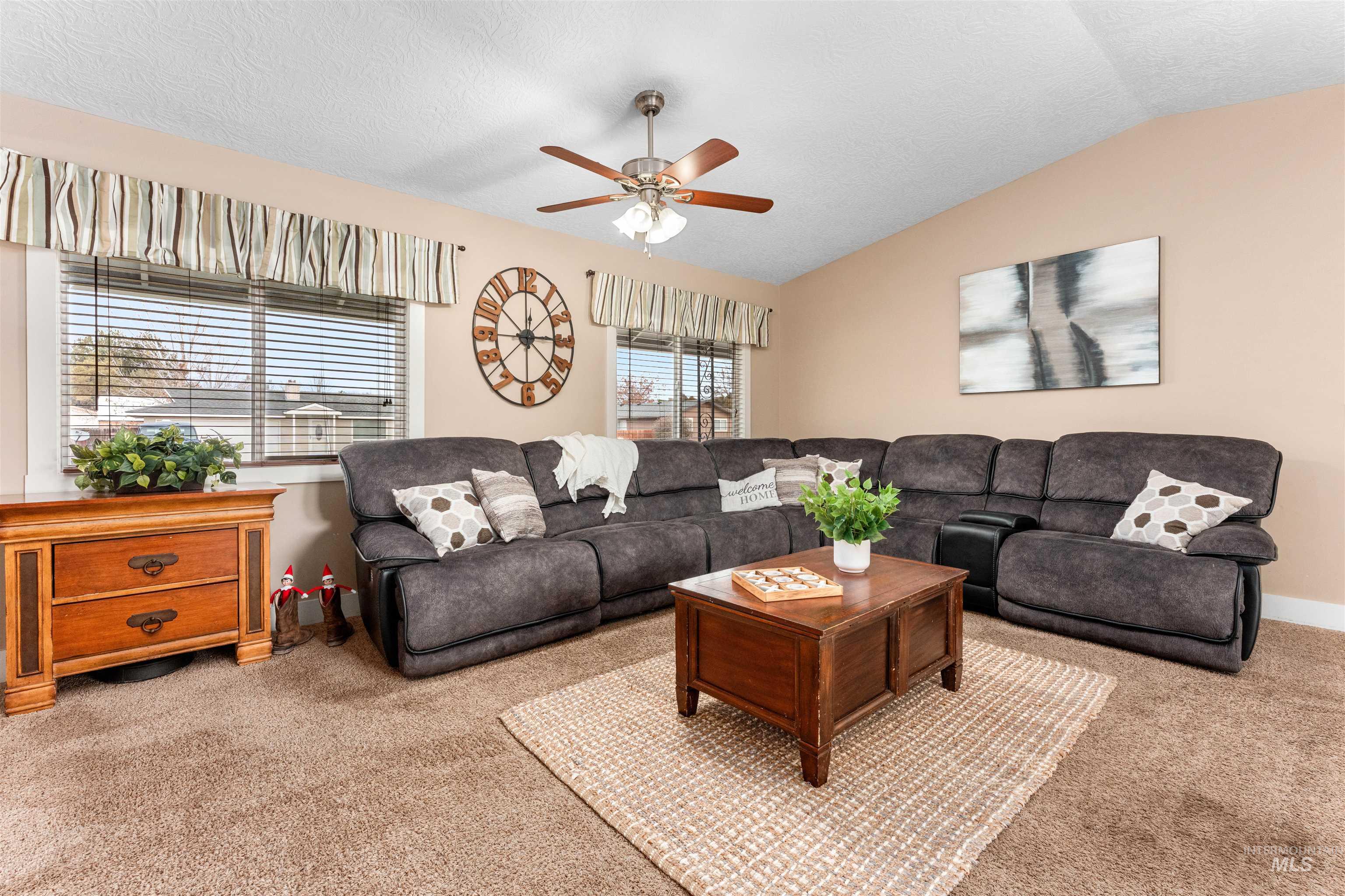 Living area with lofted ceiling, a ceiling fan, carpet floors, and a textured ceiling