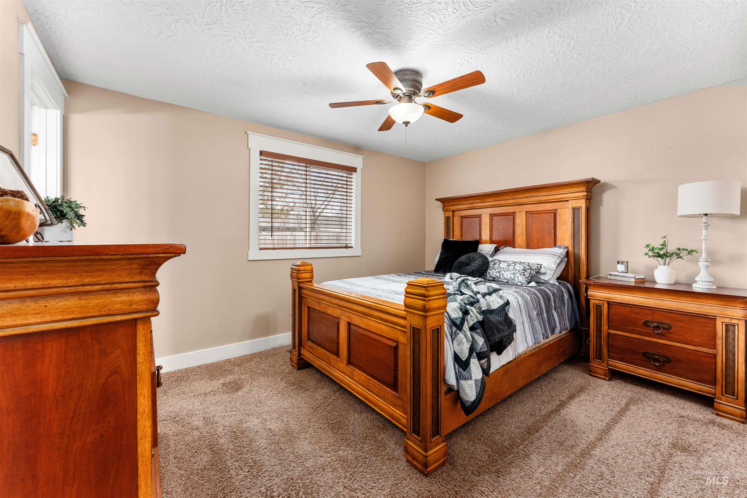 Bedroom with light colored carpet, ceiling fan, and a textured ceiling