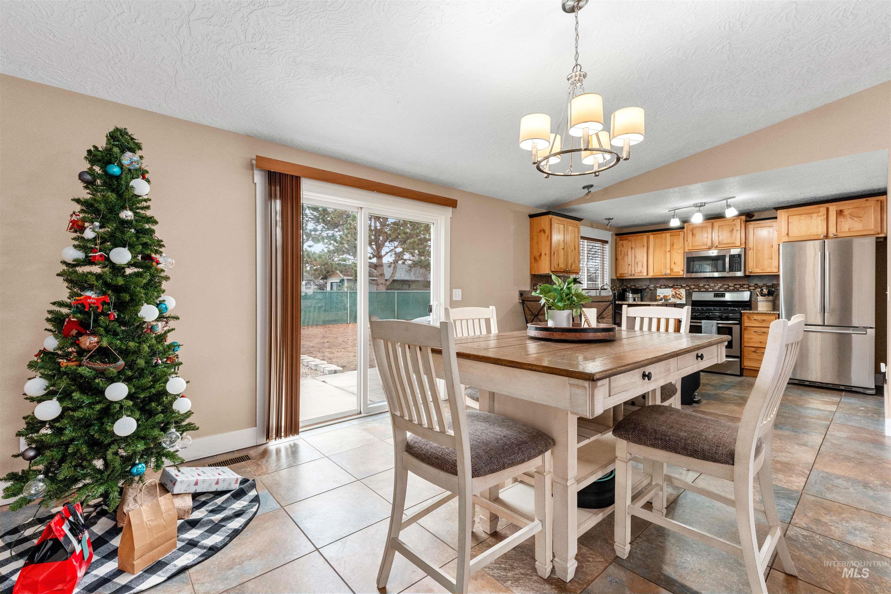Dining room with a textured ceiling, lofted ceiling, a chandelier, and light tile patterned floors
