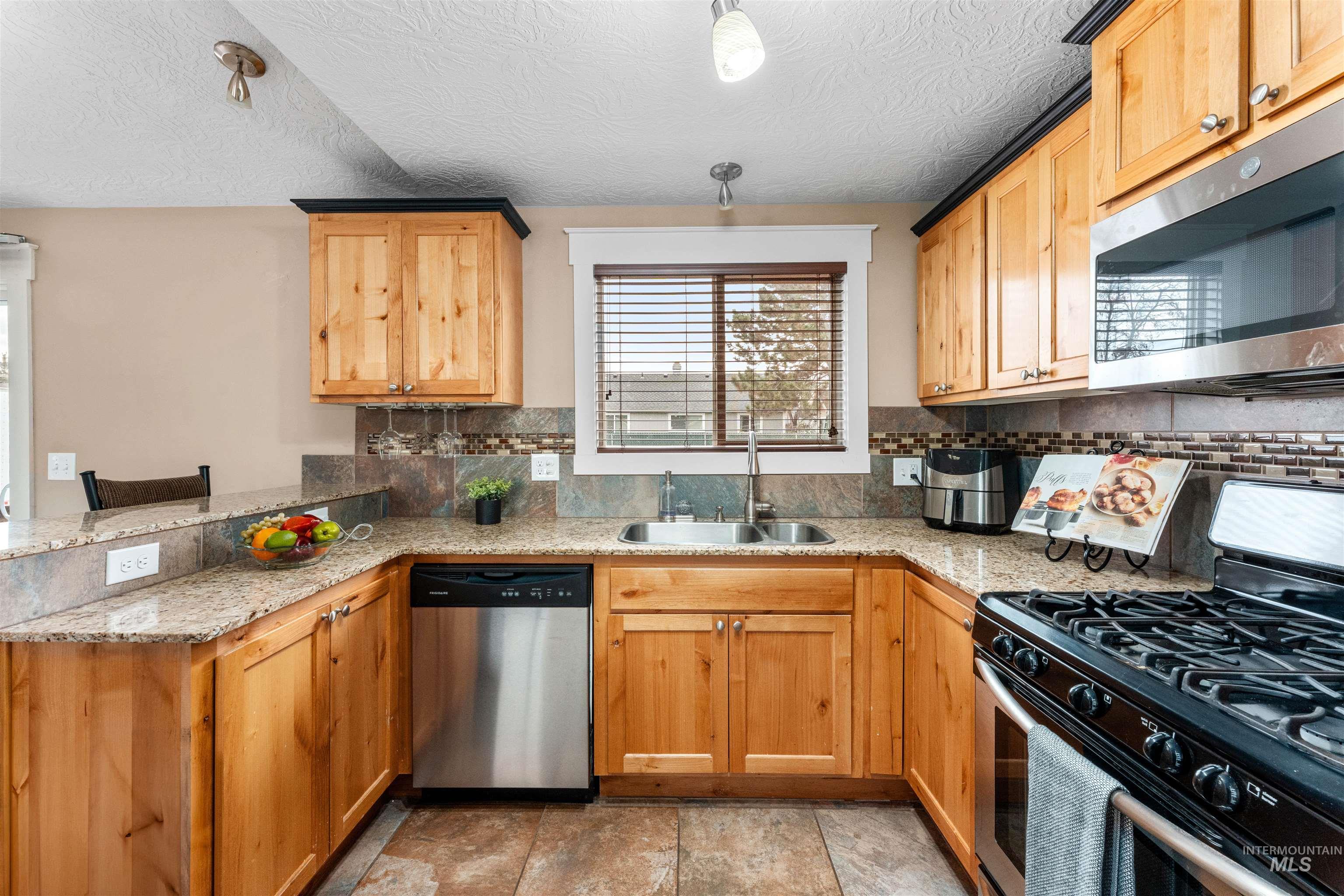 Kitchen with stainless steel appliances, light stone countertops, a peninsula, pendant lighting, and a textured ceiling
