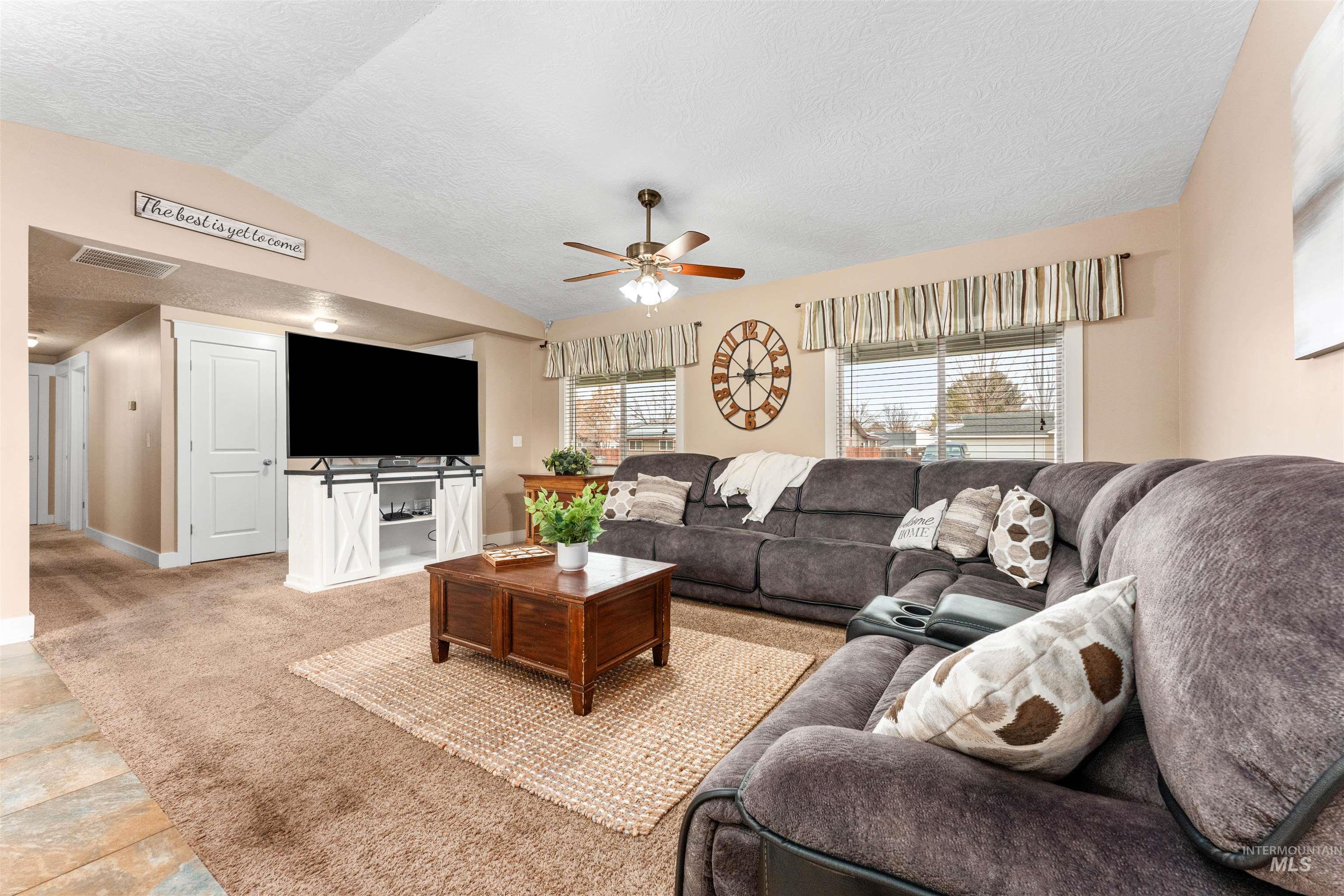 Living area featuring vaulted ceiling, a textured ceiling, light carpet, and ceiling fan